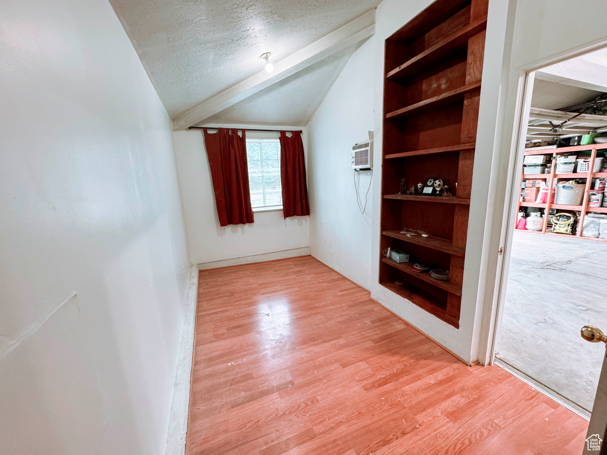 Bonus room featuring vaulted ceiling, built in features, light wood-type flooring, a wall unit AC, and a textured ceiling