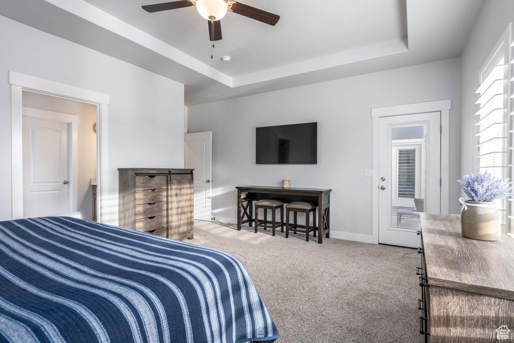 Bedroom with light carpet, ceiling fan, multiple windows, and a raised ceiling