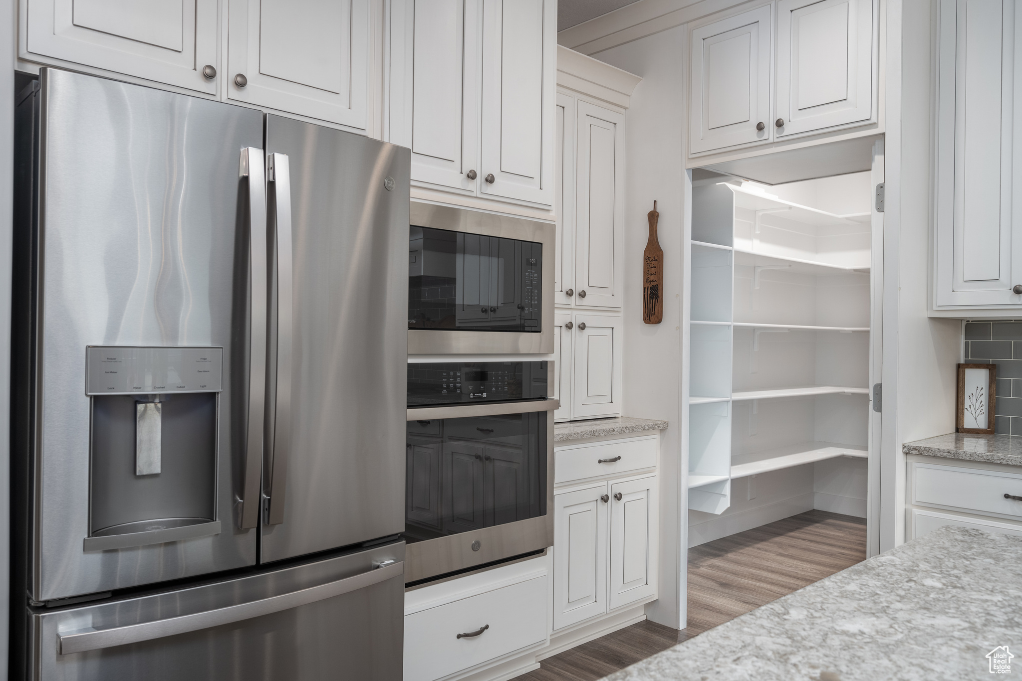 Kitchen with white cabinetry, appliances with stainless steel finishes, light stone counters, hardwood / wood-style floors, and backsplash