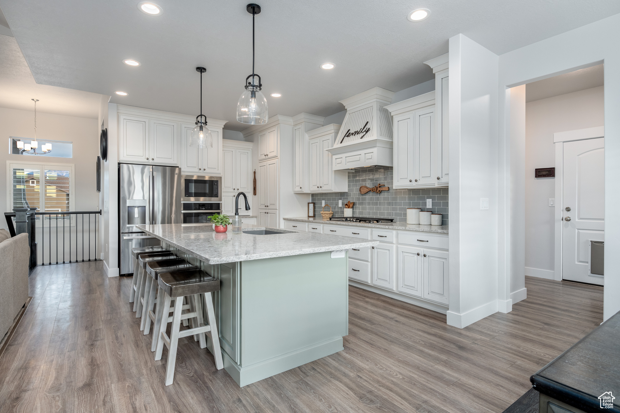 Kitchen featuring custom range hood, light hardwood / wood-style floors, a breakfast bar area, white cabinetry, and appliances with stainless steel finishes