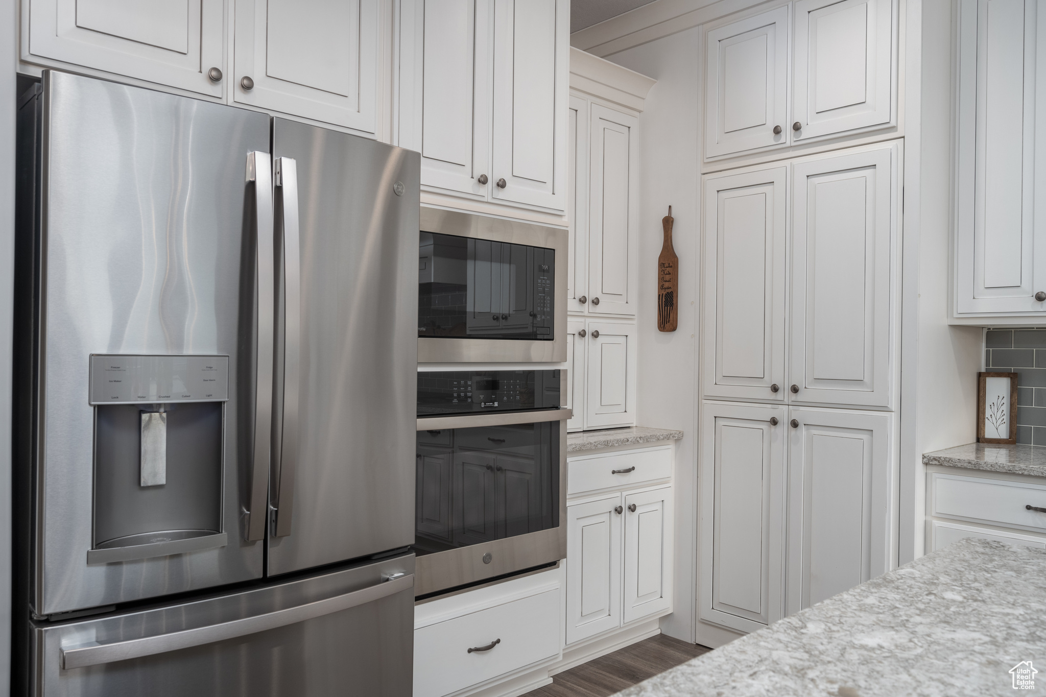 Kitchen with stainless steel appliances, dark wood-type flooring, light stone counters, and white cabinetry