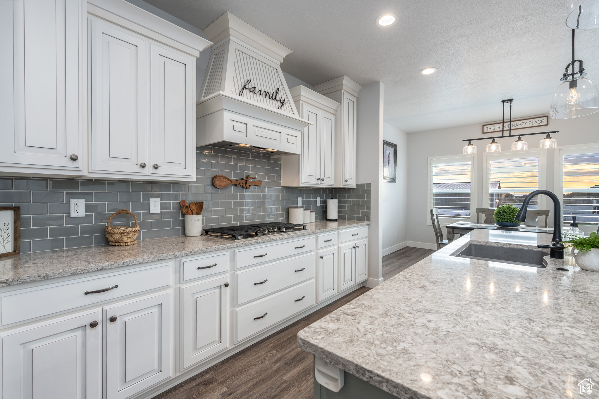 Kitchen with dark hardwood / wood-style floors, decorative light fixtures, white cabinetry, and backsplash