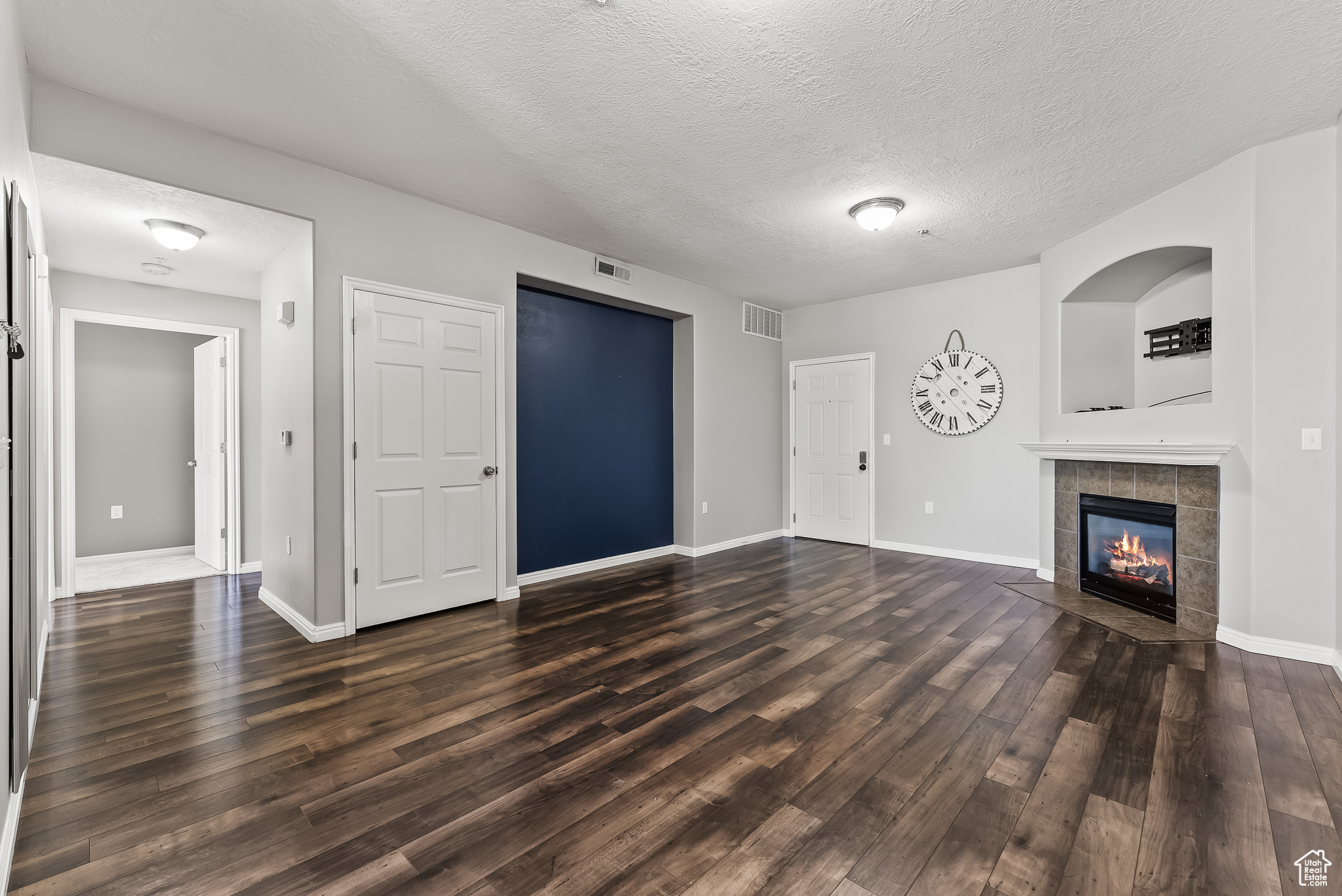 Unfurnished living room featuring a tiled fireplace, dark hardwood / wood-style flooring, and a textured ceiling