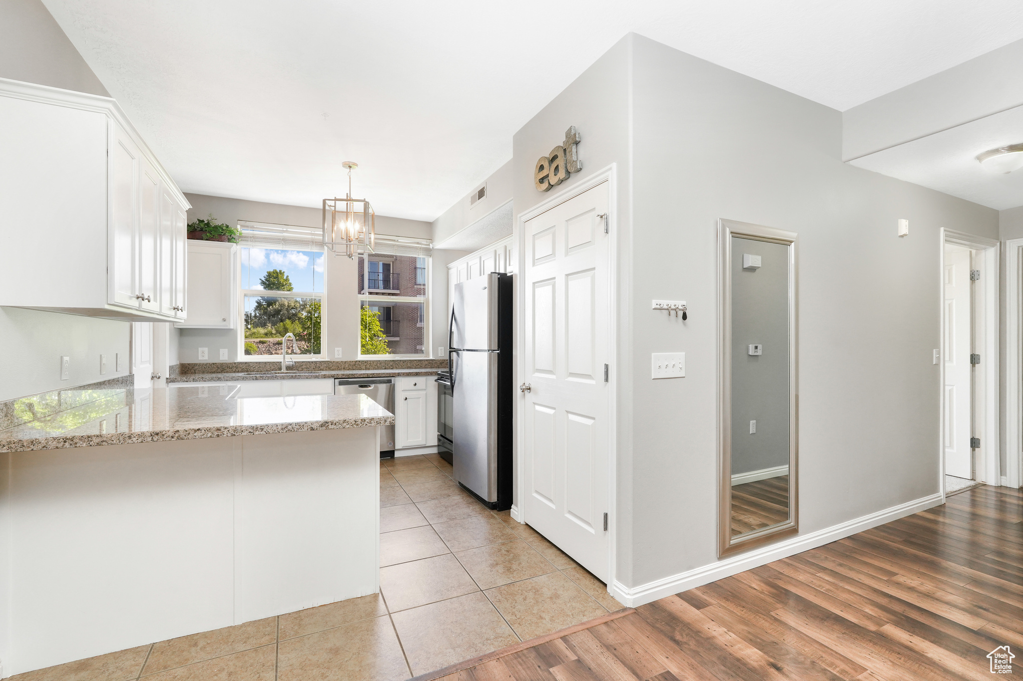 Kitchen featuring light stone counters, kitchen peninsula, white cabinets, light tile floors, and appliances with stainless steel finishes