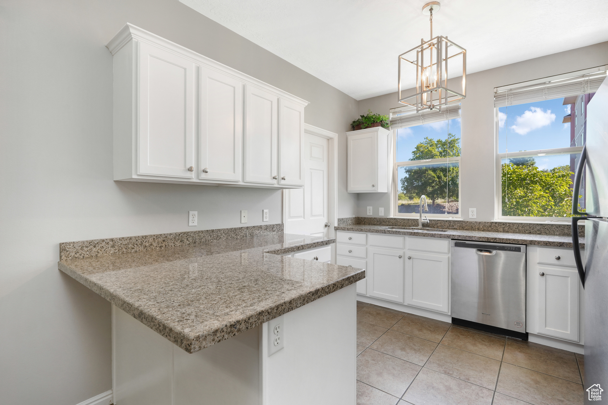 Kitchen featuring a chandelier, light tile flooring, kitchen peninsula, stainless steel appliances, and white cabinetry