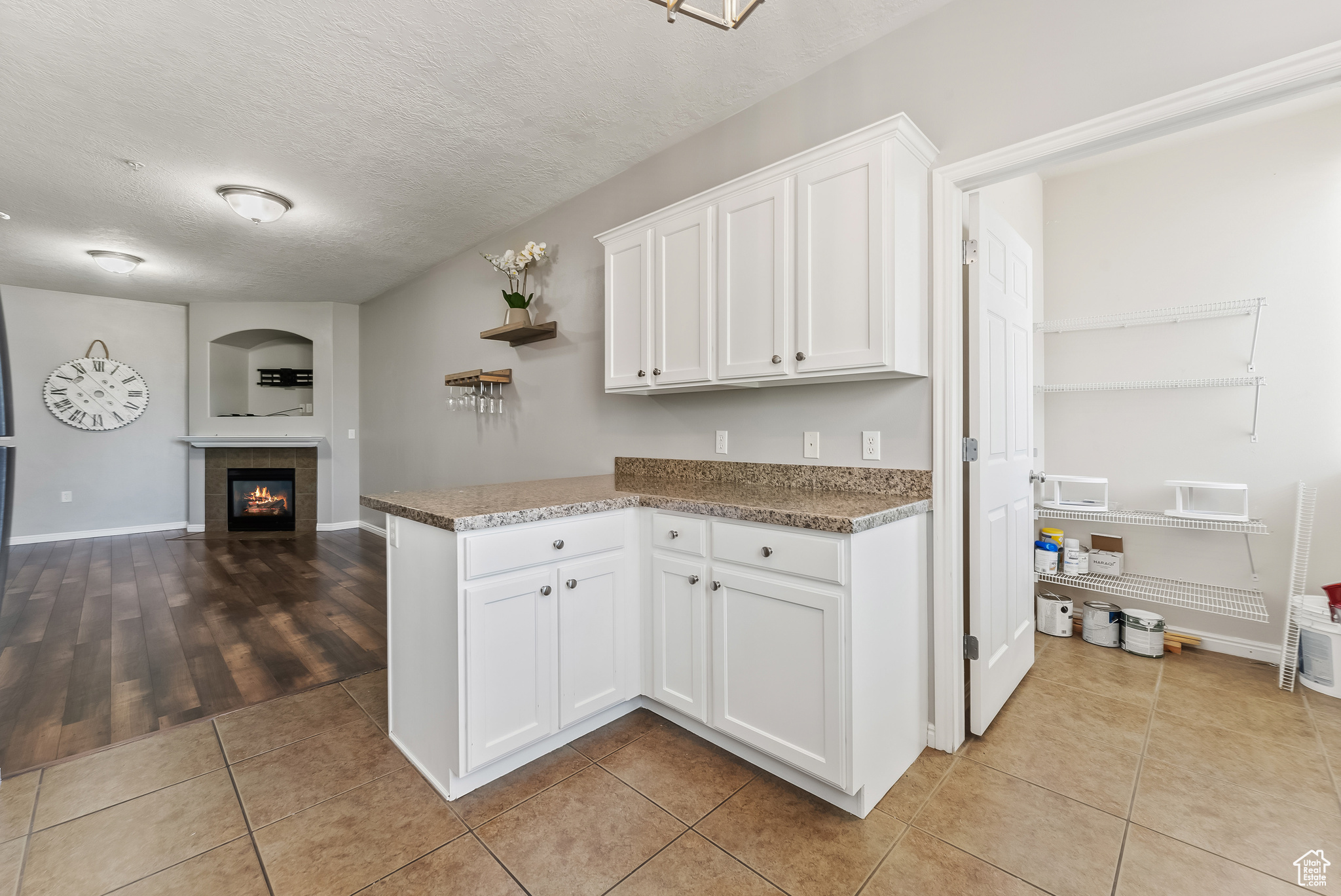 Kitchen with white cabinetry, a tiled fireplace, light tile flooring, and a textured ceiling with huge storage room off the kitchen