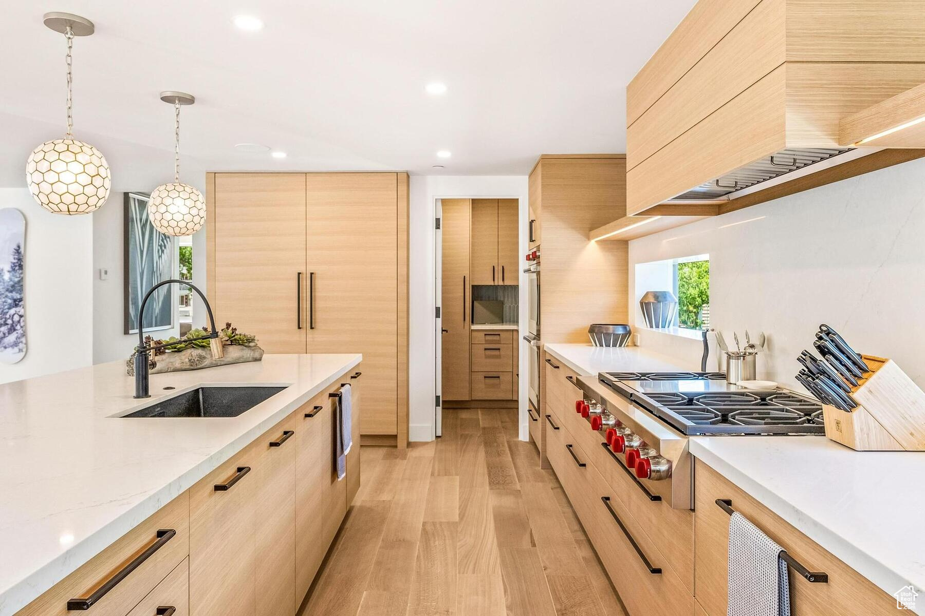 Kitchen featuring decorative light fixtures, custom range hood, light hardwood / wood-style floors, light brown cabinetry, and sink