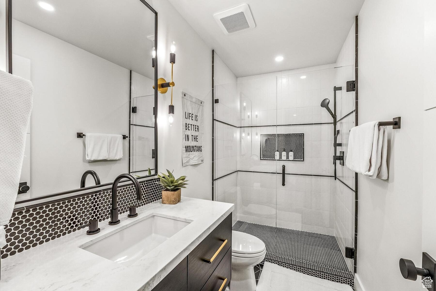 Bathroom featuring a shower with shower door, backsplash, oversized vanity, and toilet