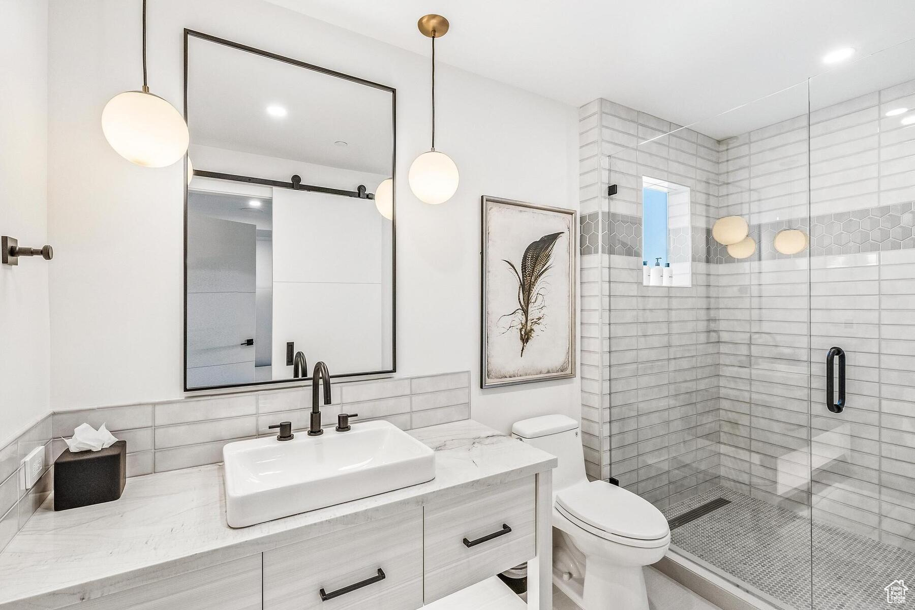 Bathroom featuring a shower with shower door, backsplash, vanity, and toilet