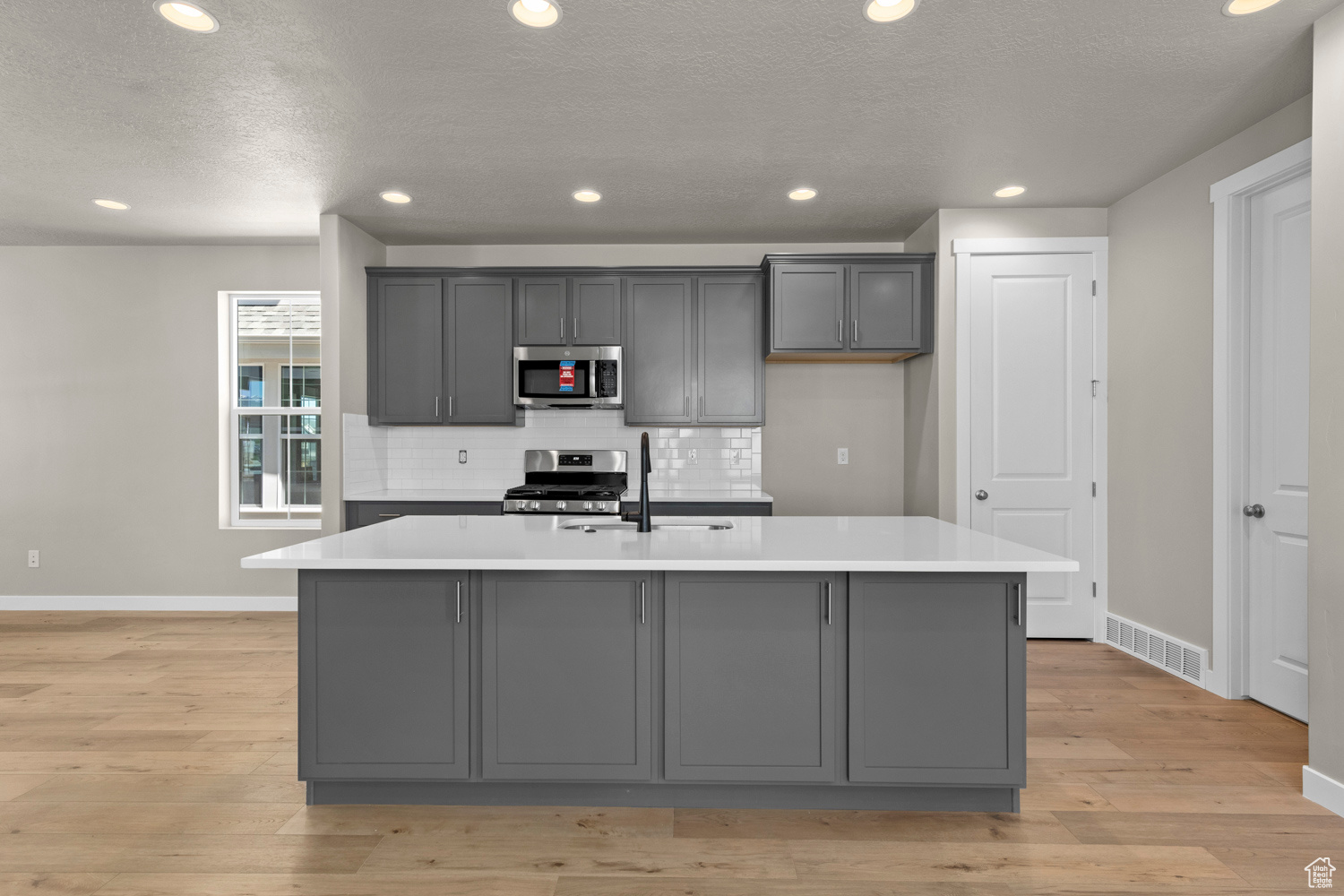 Kitchen with stainless steel appliances, gray cabinetry, light hardwood / wood-style flooring, and a kitchen island with sink