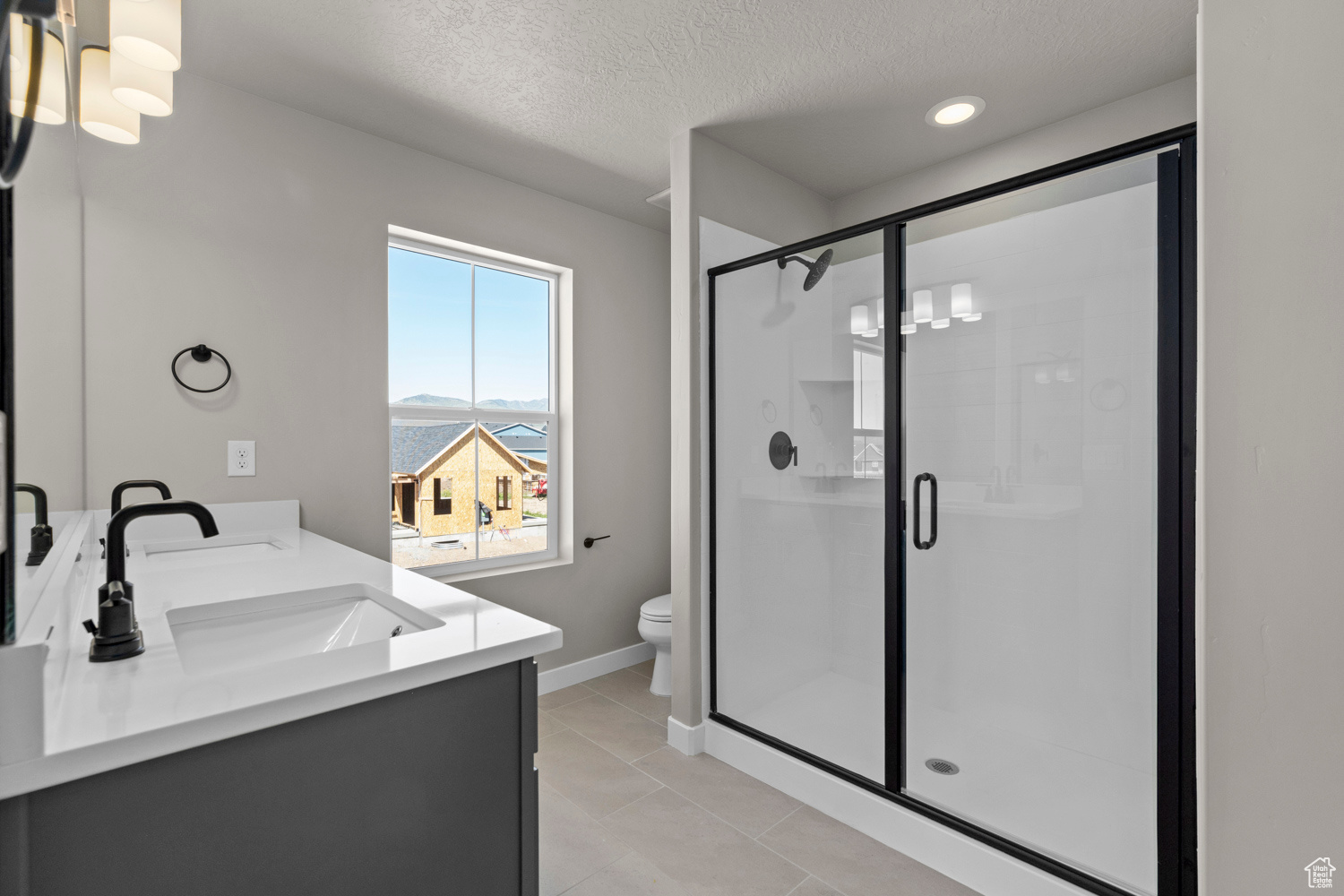 Bathroom with a shower with door, double sink vanity, tile floors, and toilet