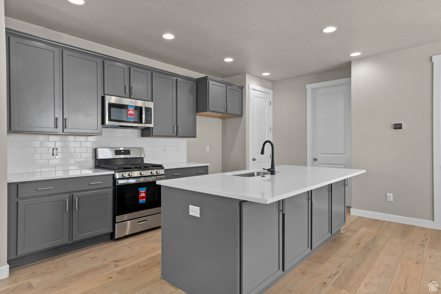 Kitchen with appliances with stainless steel finishes, light hardwood / wood-style floors, a kitchen island with sink, and sink