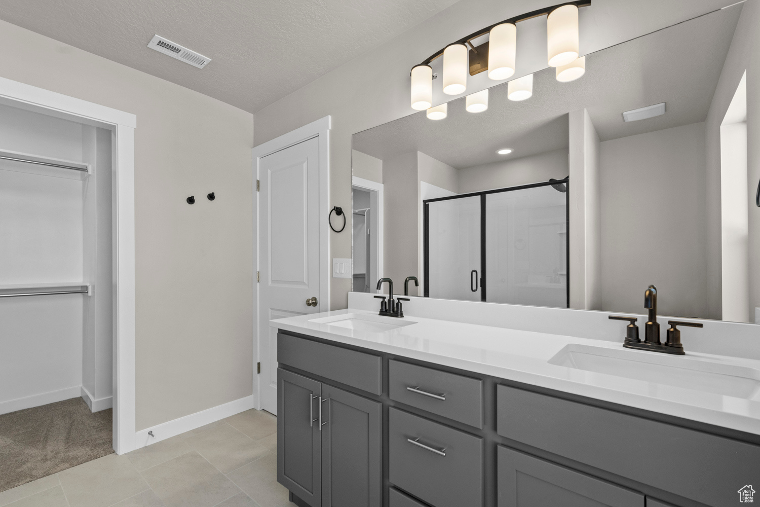 Bathroom with dual vanity, an enclosed shower, and tile floors