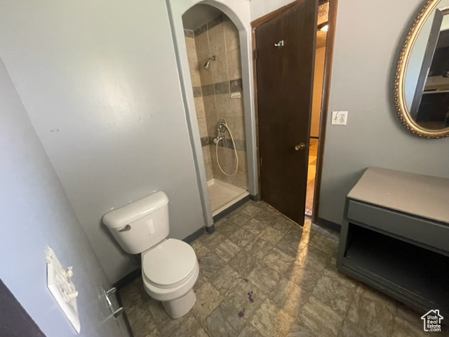 Bathroom featuring a tile shower, vanity, toilet, and tile floors