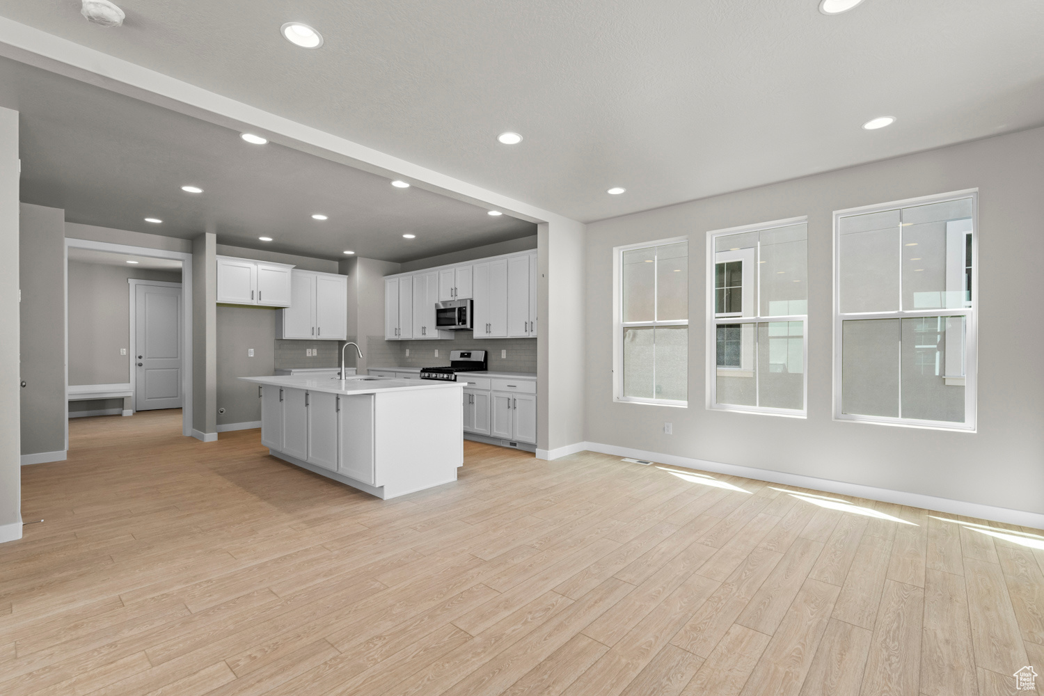 Kitchen featuring light hardwood / wood-style floors, stainless steel appliances, white cabinetry, an island with sink, and sink