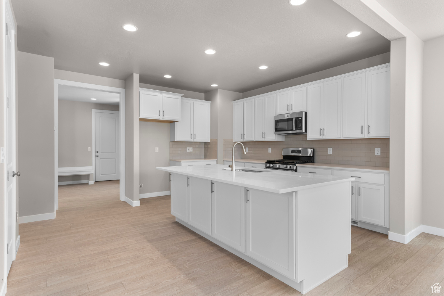 Kitchen featuring a center island with sink, light hardwood / wood-style flooring, appliances with stainless steel finishes, sink, and tasteful backsplash