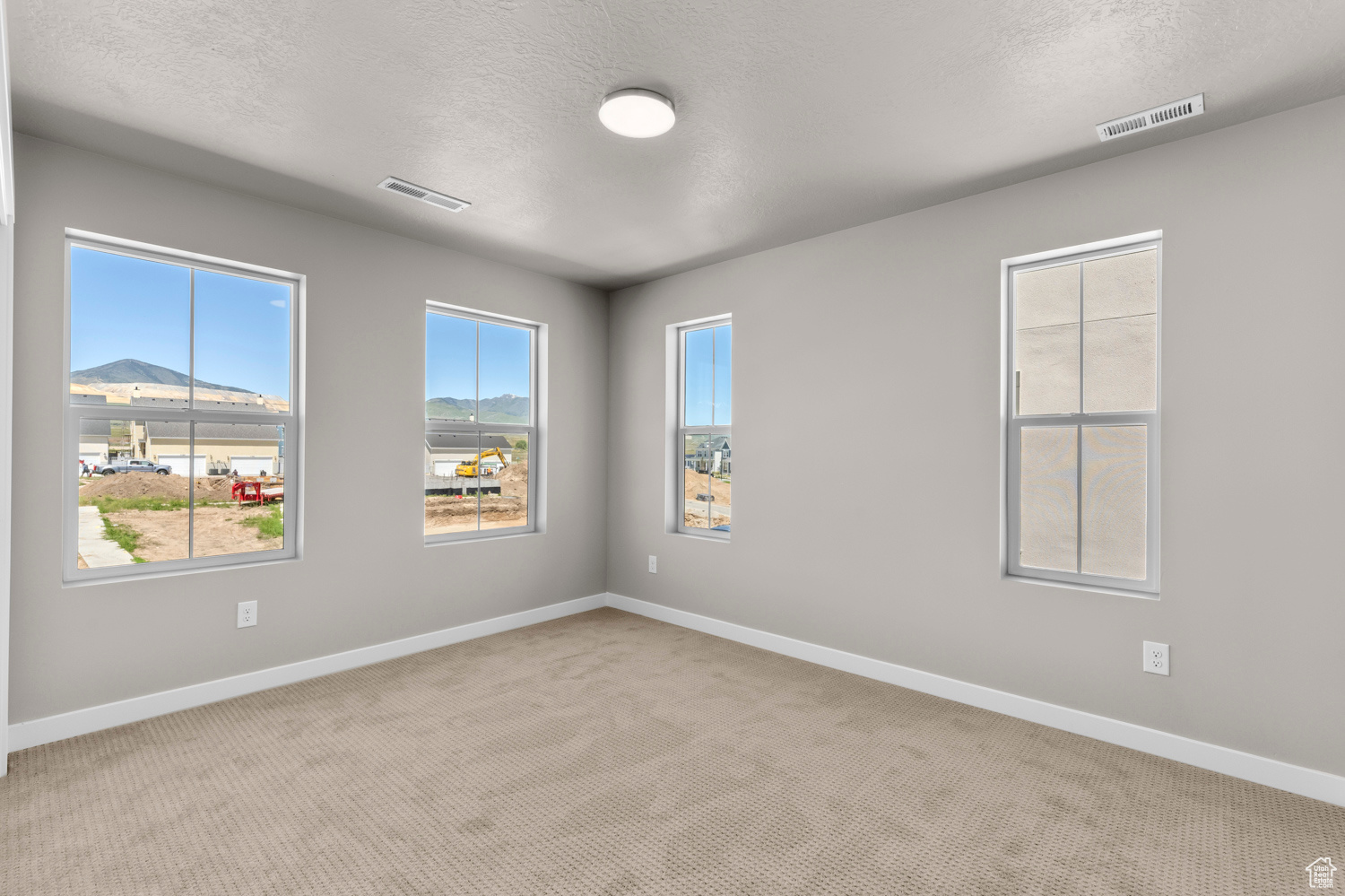 Carpeted empty room with a textured ceiling and plenty of natural light