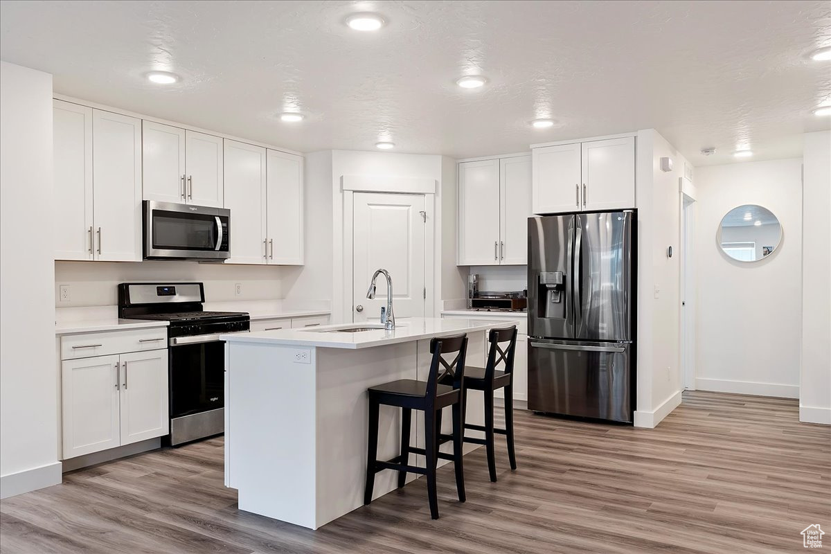 Kitchen with appliances with stainless steel finishes, sink, white cabinets, and wood-type flooring