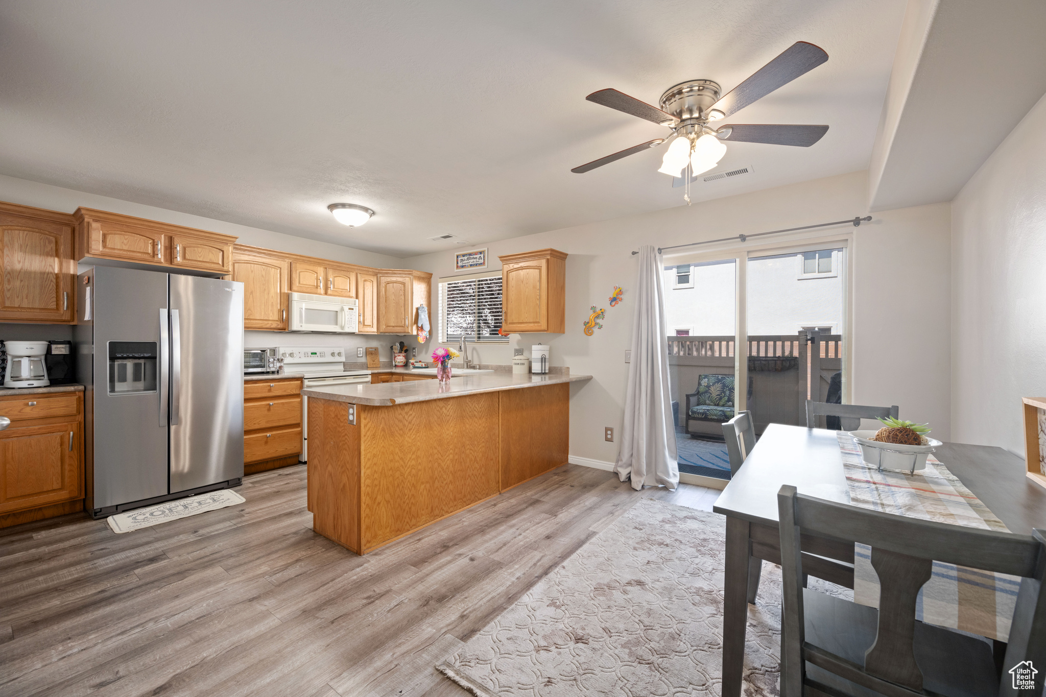 Kitchen with light hardwood / wood-style floors, ceiling fan, white appliances, and kitchen peninsula