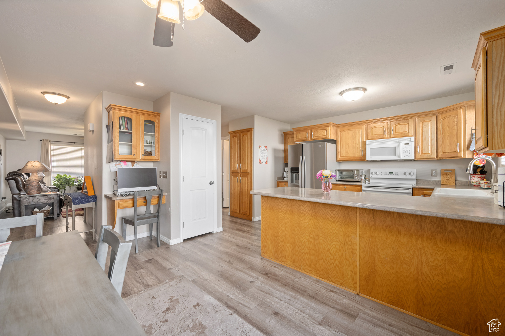 Kitchen featuring light hardwood / wood-style floors, white appliances, kitchen peninsula, sink, and ceiling fan