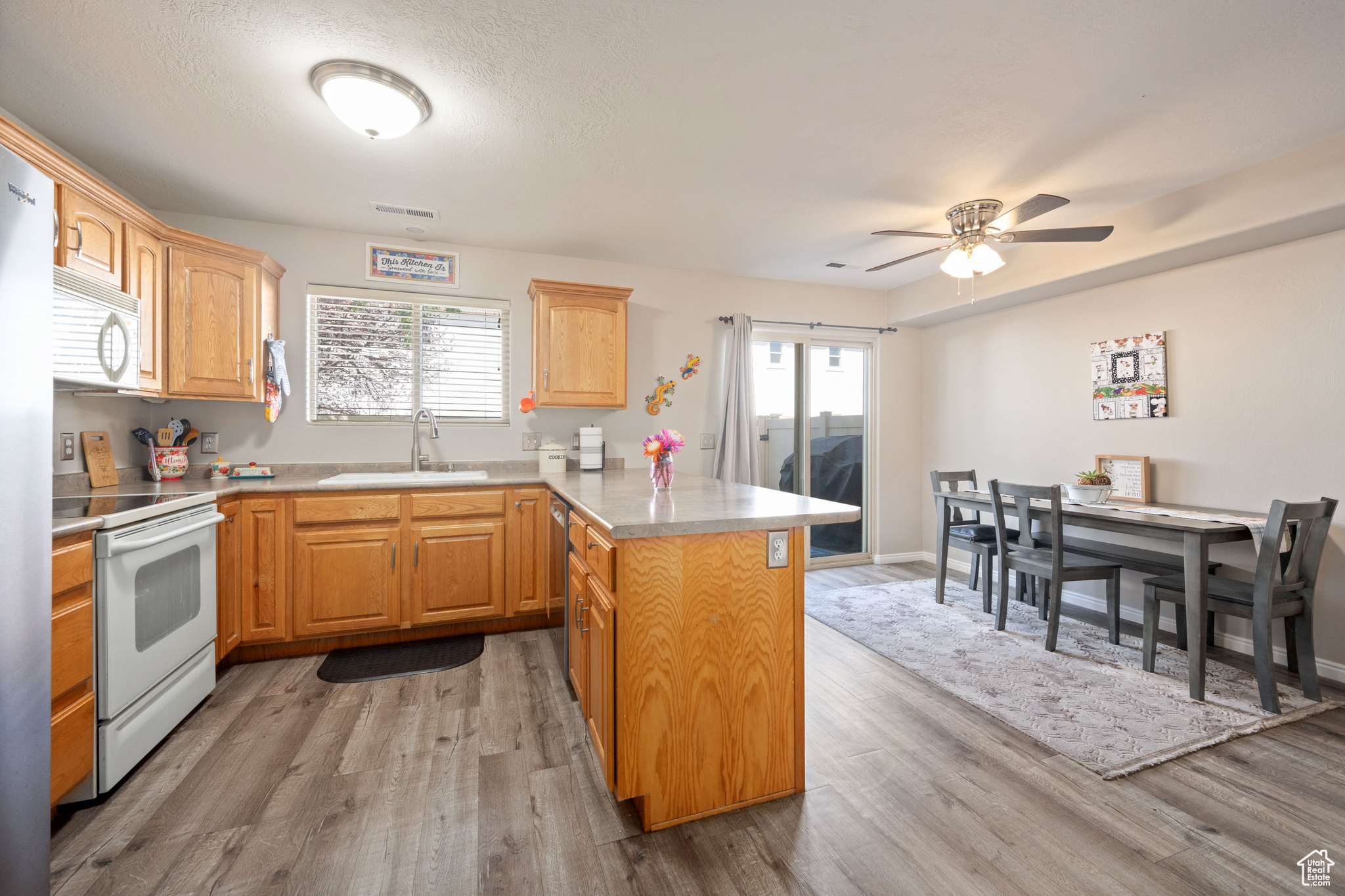 Kitchen featuring white appliances, ceiling fan, sink, and light wood-type flooring