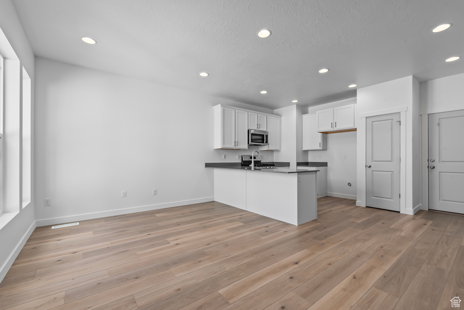 Kitchen featuring light wood-type flooring, white cabinets, and kitchen peninsula