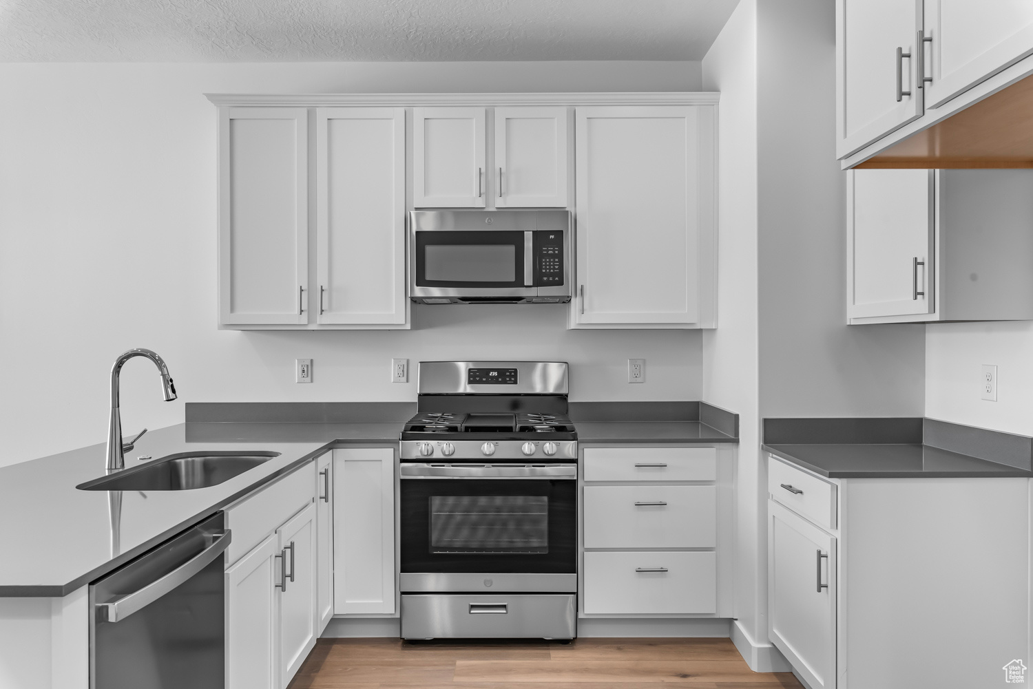 Kitchen with appliances with stainless steel finishes, light hardwood / wood-style floors, sink, and white cabinetry