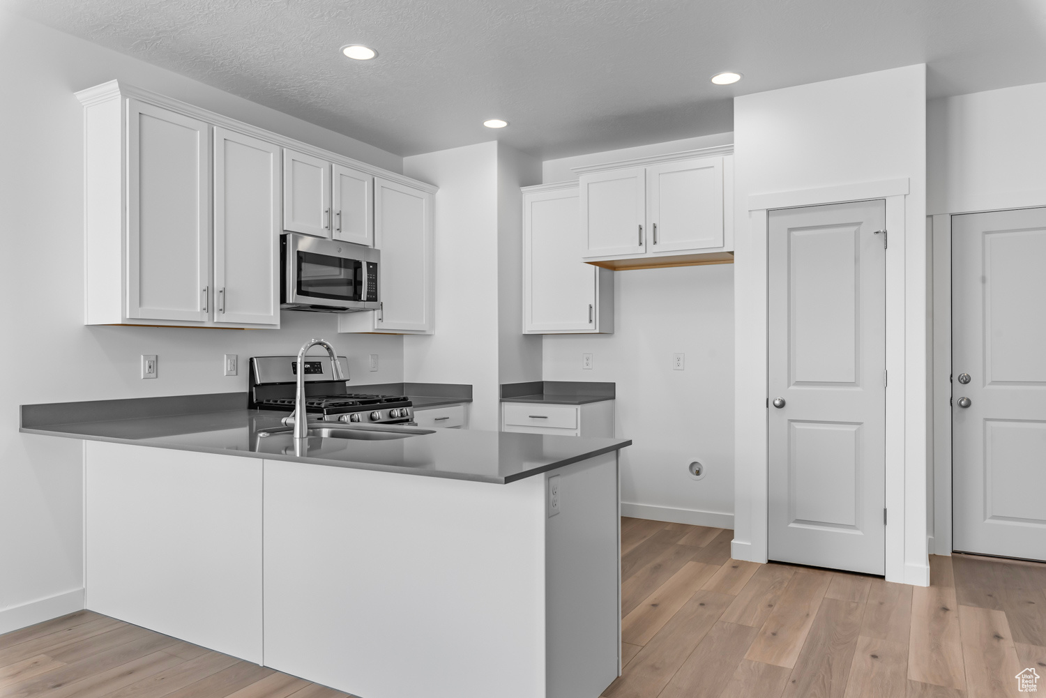 Kitchen featuring stainless steel appliances, light hardwood / wood-style flooring, kitchen peninsula, and white cabinetry