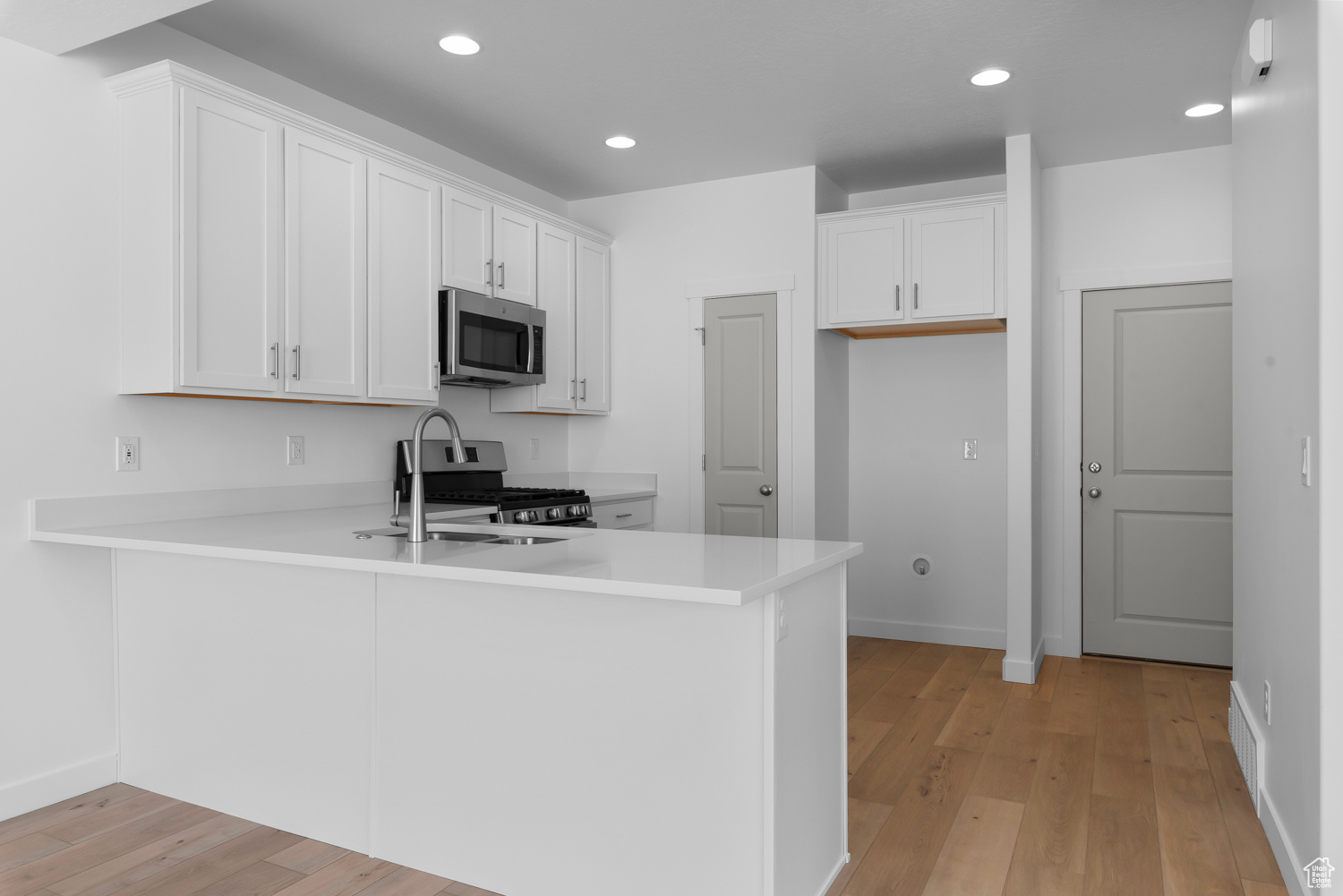 Kitchen with white cabinets, light hardwood / wood-style floors, kitchen peninsula, stainless steel appliances, and sink