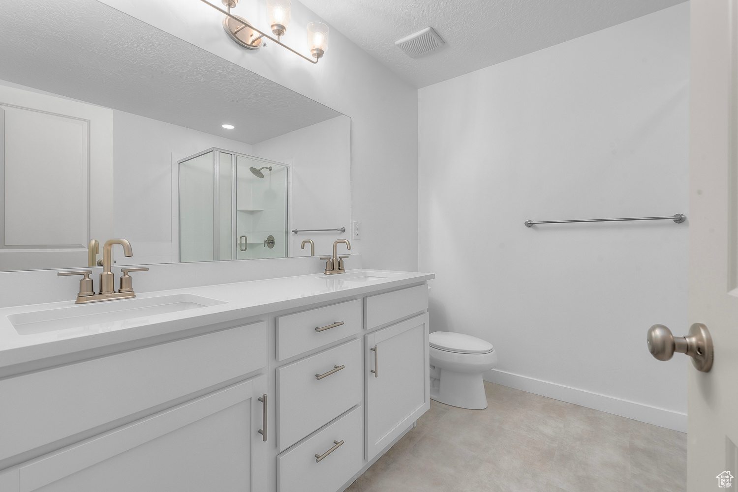 Bathroom featuring a textured ceiling, tile floors, large vanity, toilet, and dual sinks