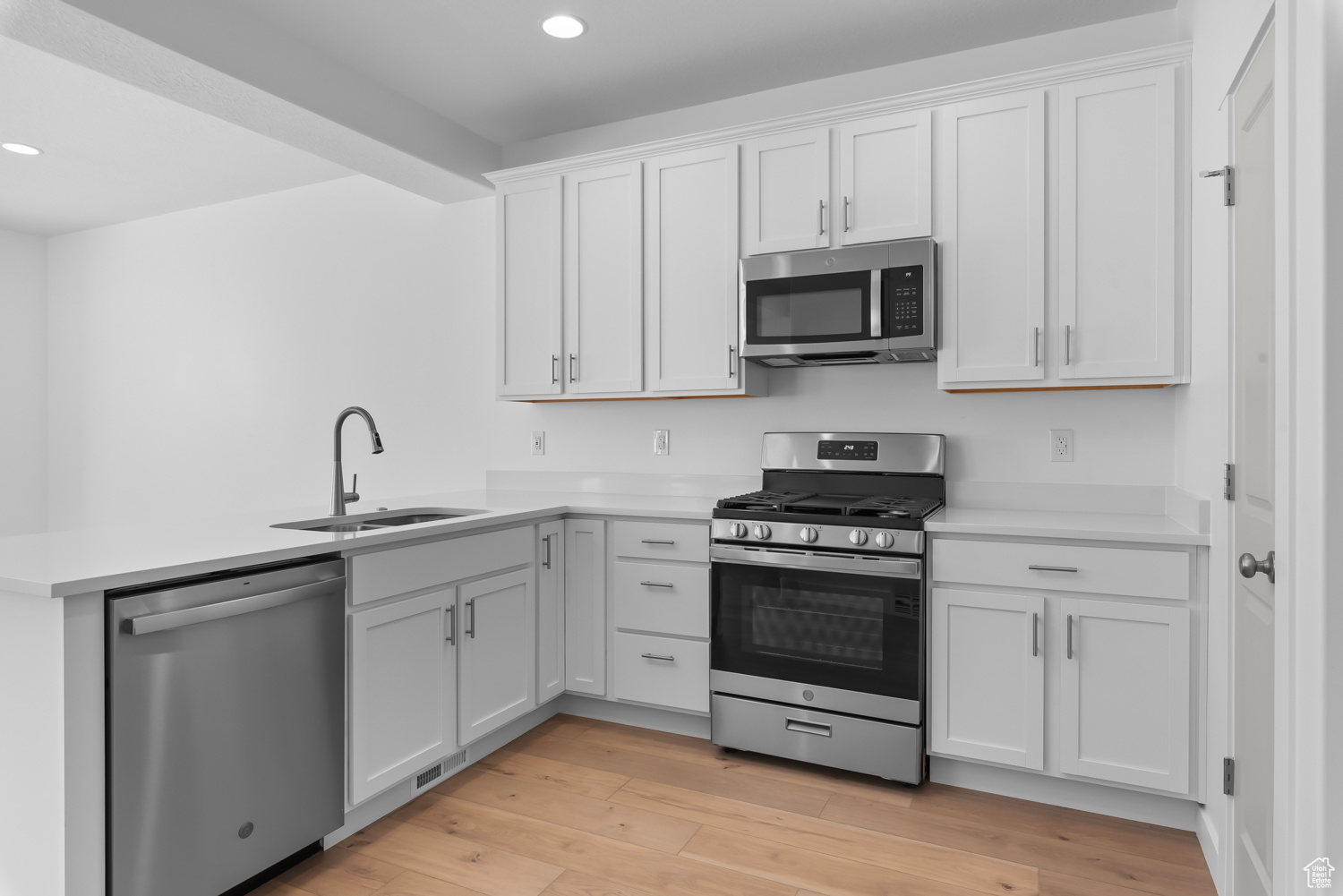 Kitchen featuring light hardwood / wood-style floors, stainless steel appliances, beamed ceiling, white cabinets, and sink