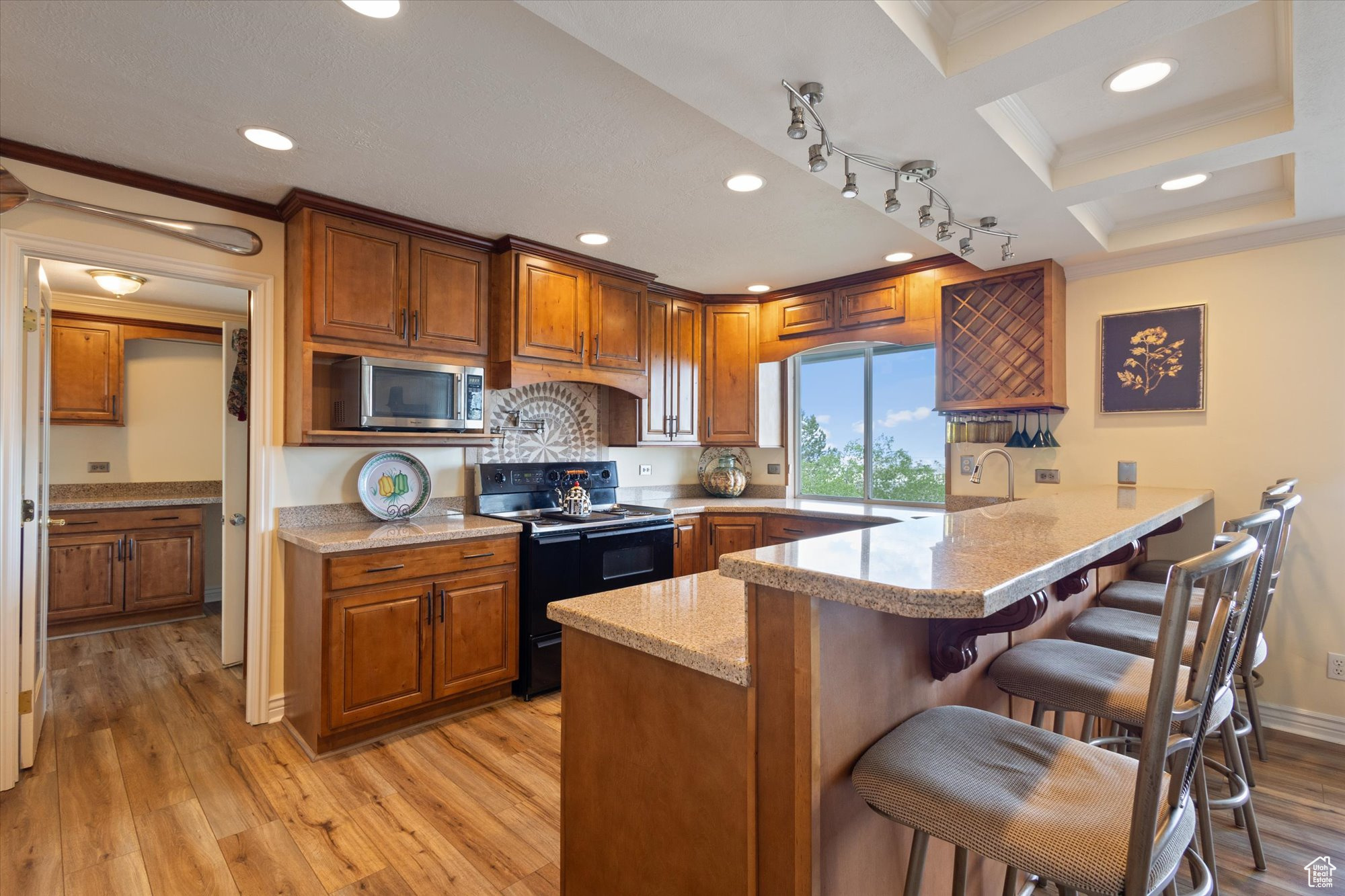 Kitchen with granite counters, coffered ceiling, a kitchen breakfast bar, black range with electric/gas stovetop, and light wood-type flooring