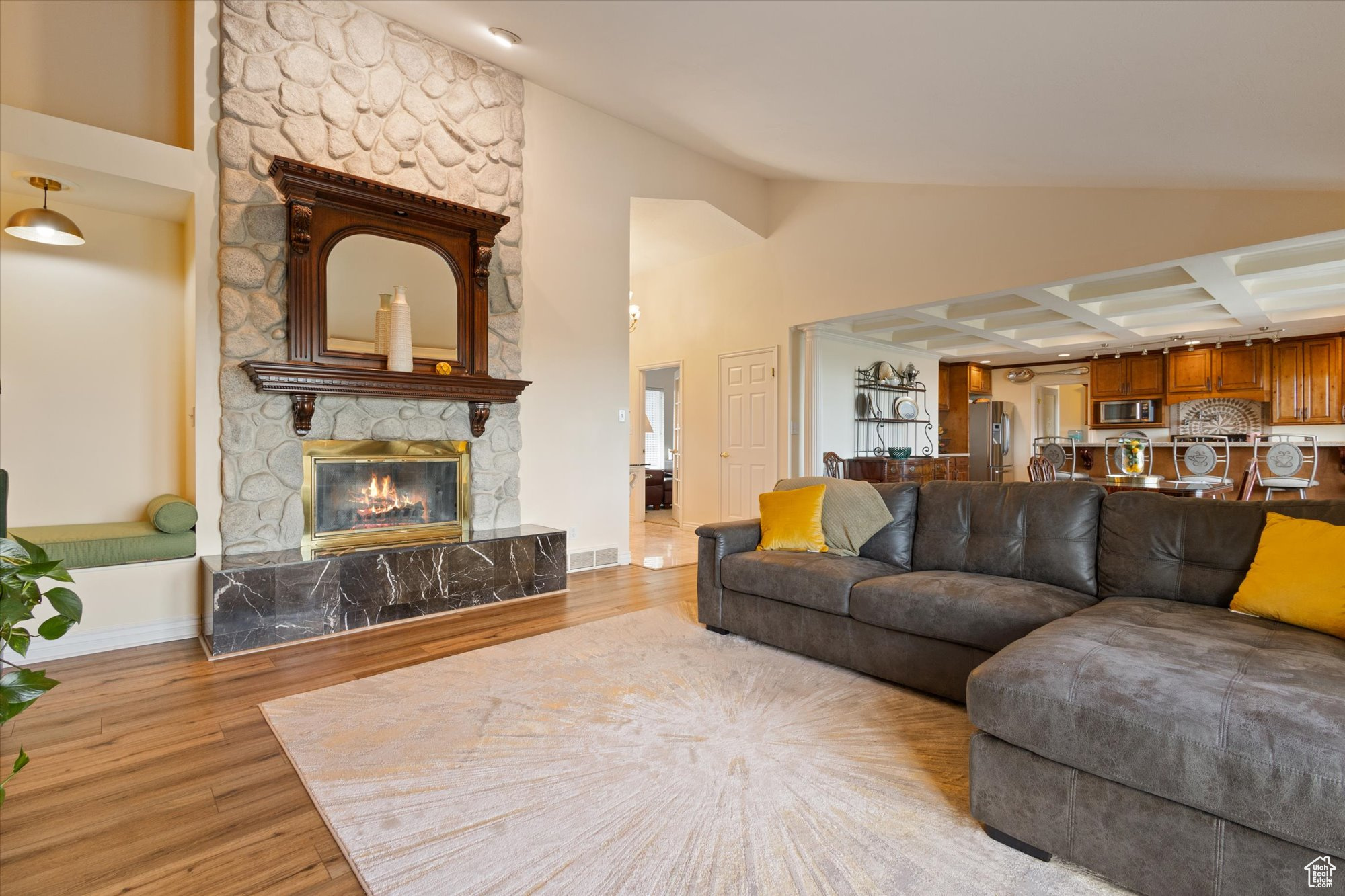 Living room featuring coffered ceiling, light hardwood / wood-style flooring, a floor to ceiling stone fireplace, and vaulted ceiling.