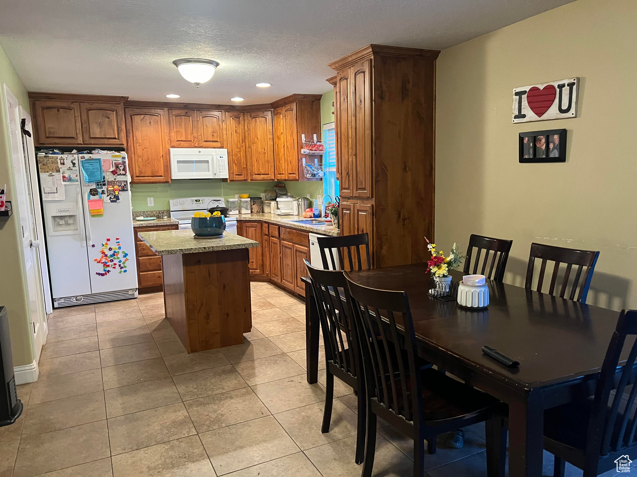 Kitchen with white appliances, light tile flooring, a textured ceiling, a center island, and sink