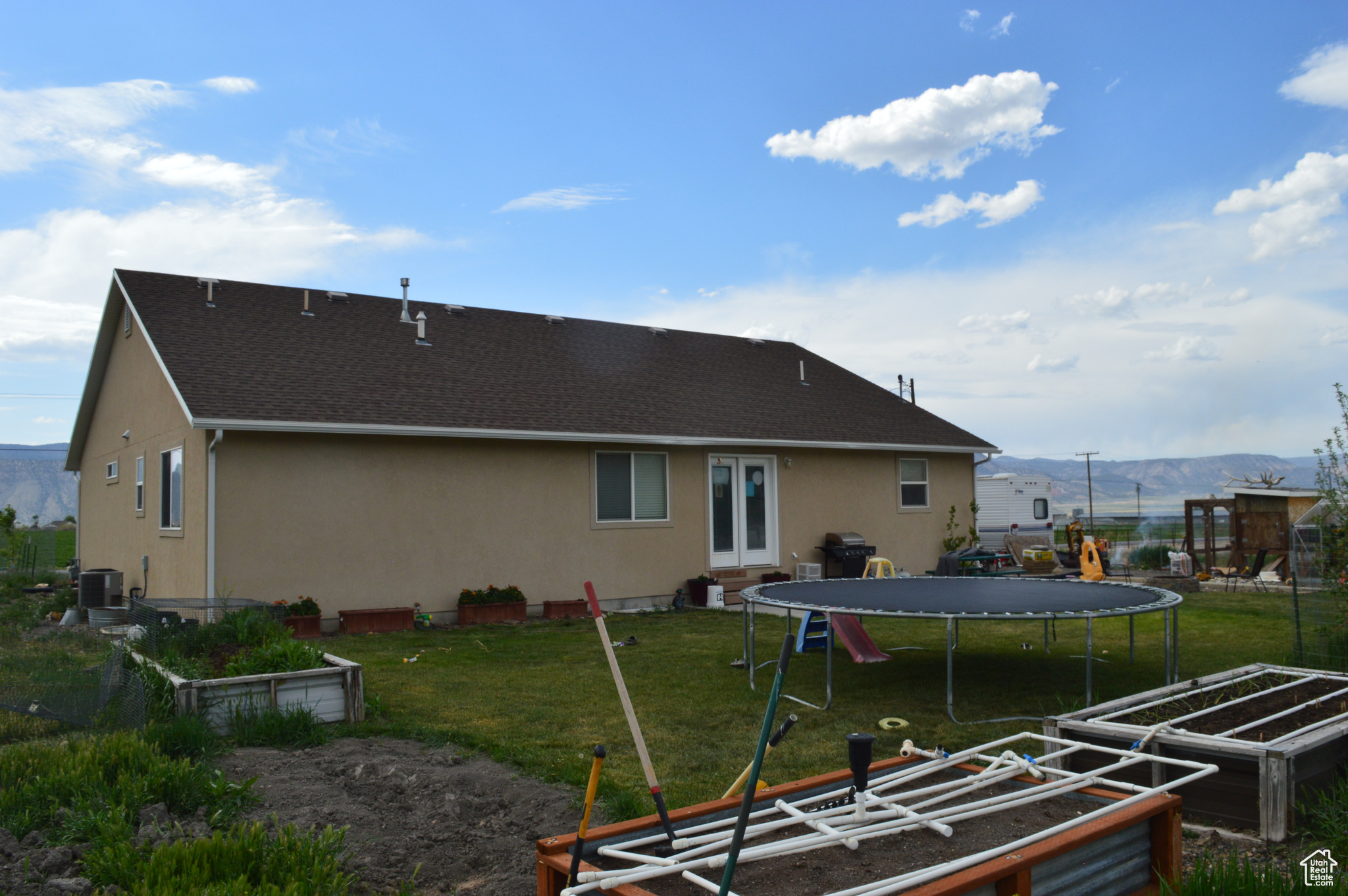 Back of property featuring a lawn, central AC unit, a trampoline, and a mountain view