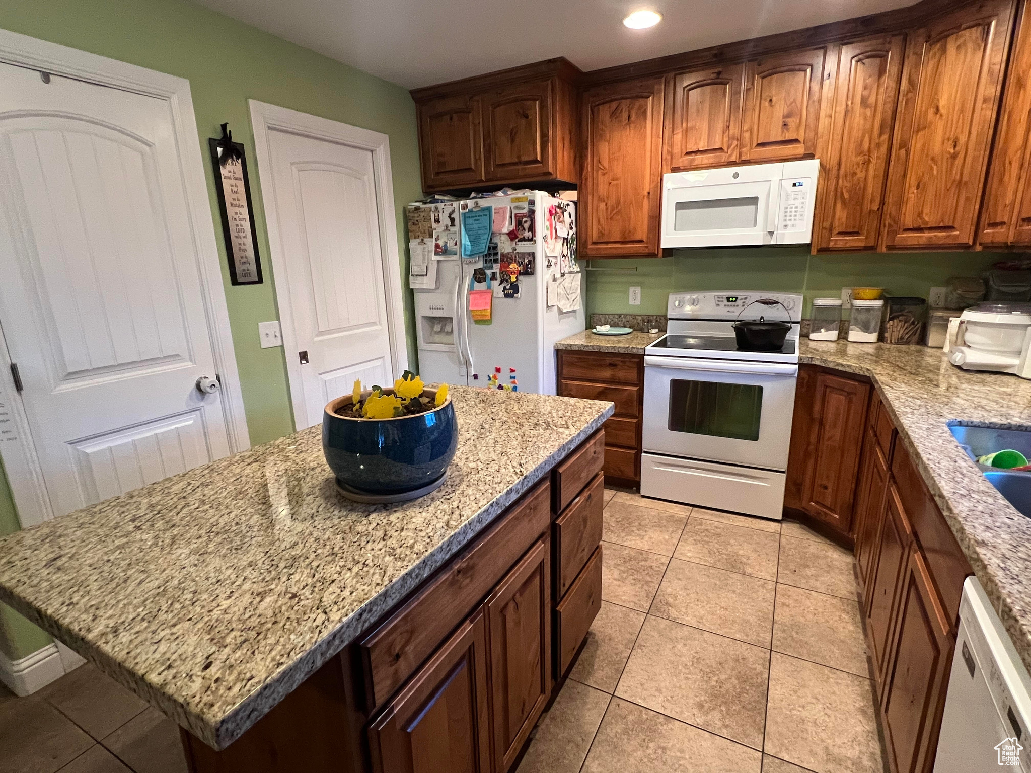 Kitchen with white appliances, light tile flooring, a kitchen island, and light stone counters