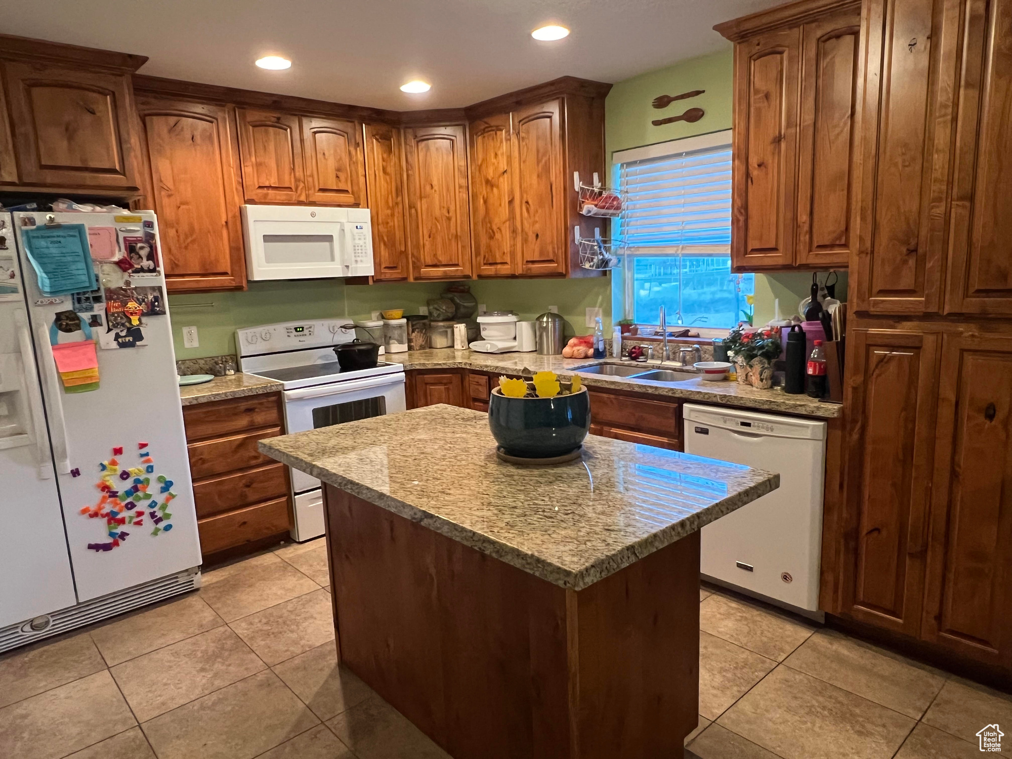 Kitchen with light stone counters, a kitchen island, sink, white appliances, and light tile floors