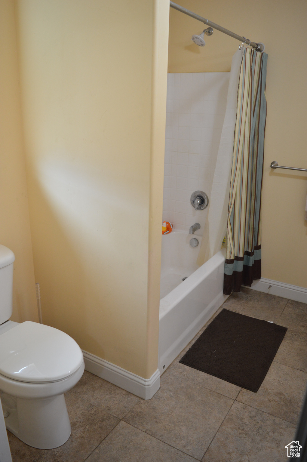 Bathroom with tile flooring, shower / bath combination with curtain, and toilet