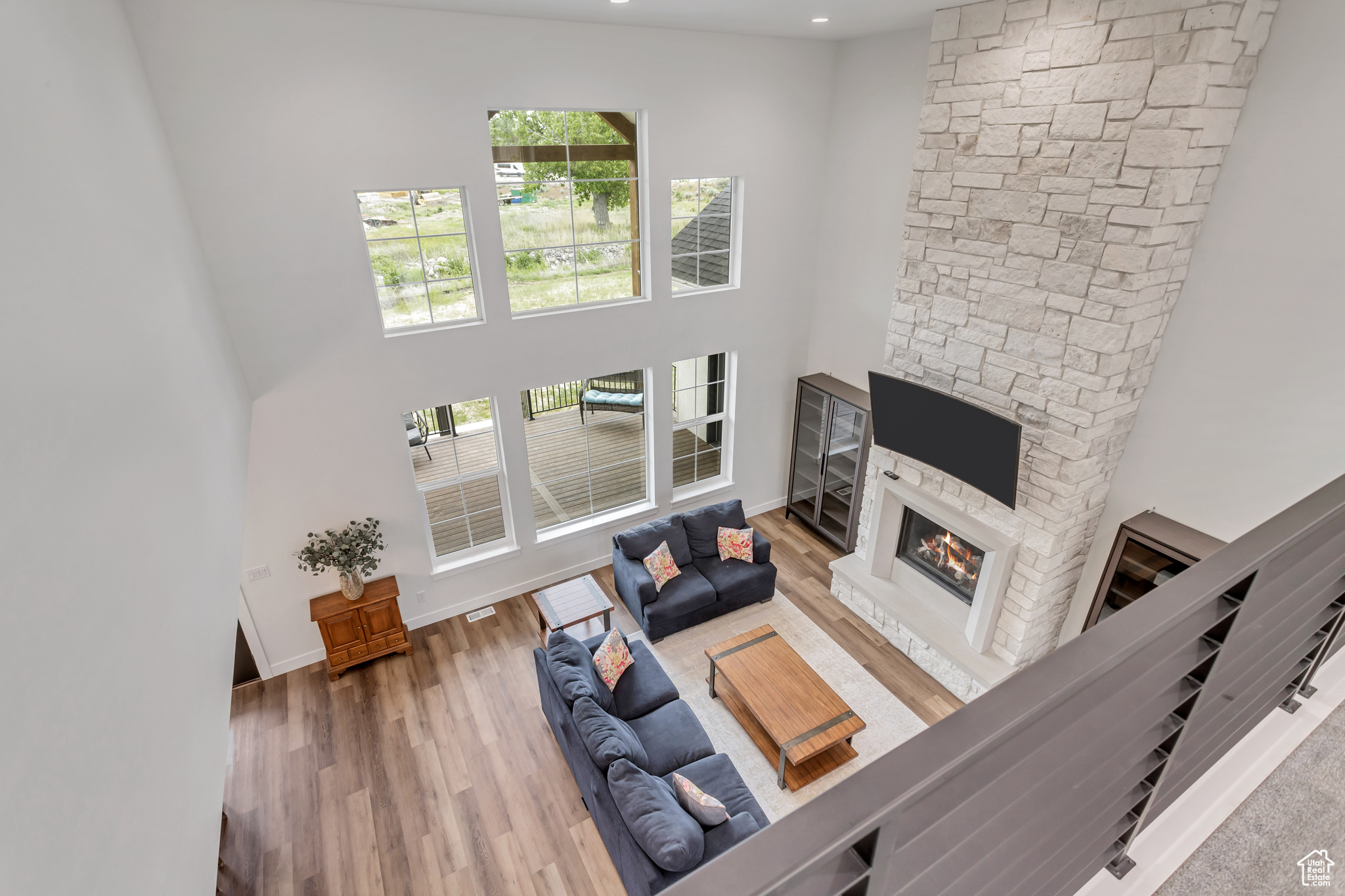 Upstairs bridge view of living room featuring a custom surround stone fireplace, a high ceiling, plenty of natural light