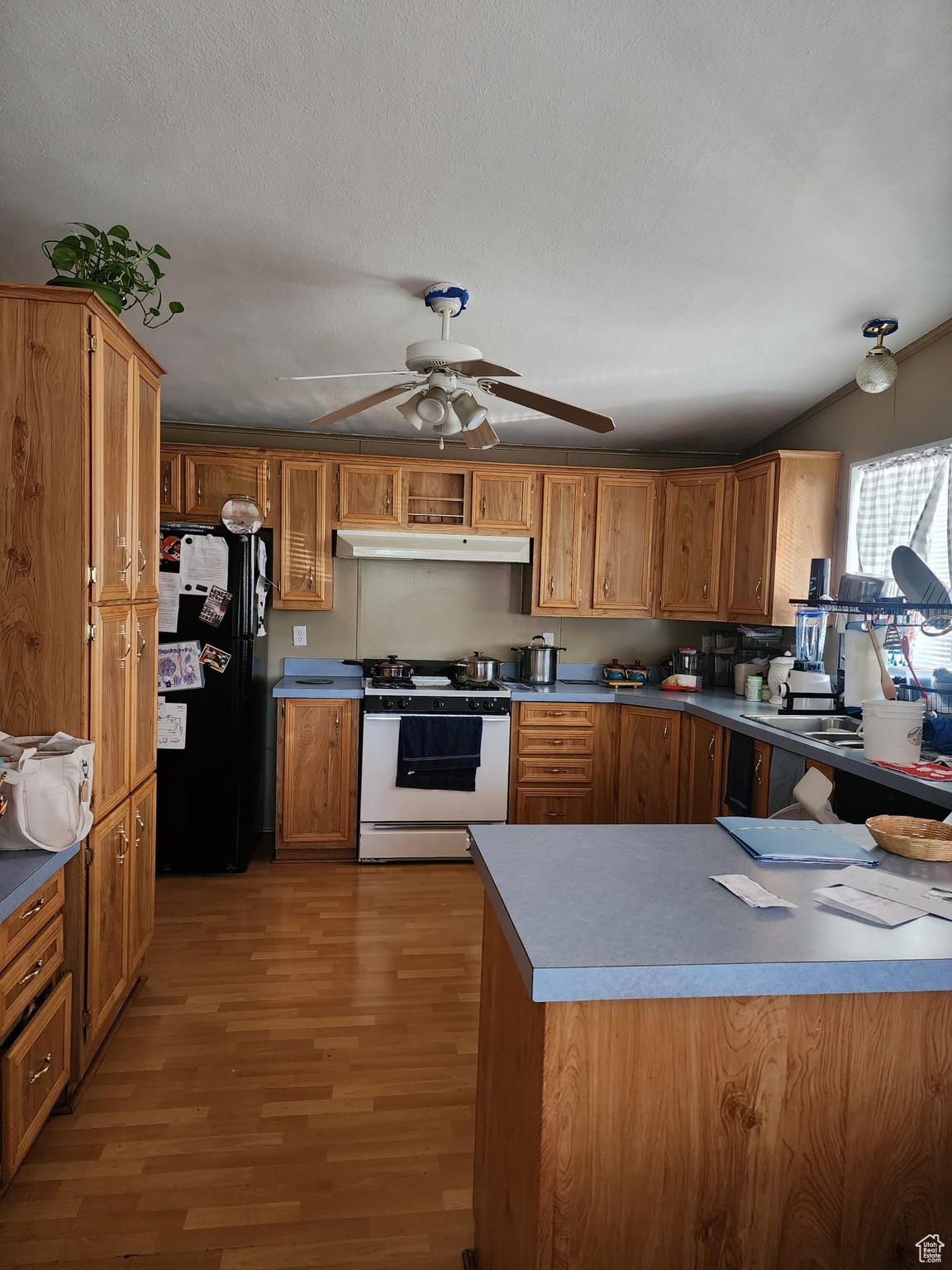 Kitchen featuring black fridge, ceiling fan, hardwood / wood-style flooring, white range with gas cooktop, and a textured ceiling