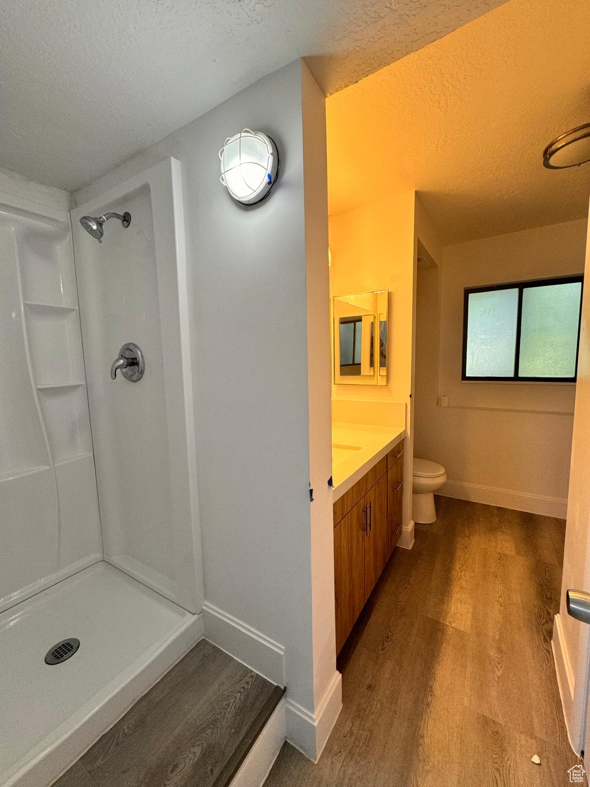 Bathroom featuring a textured ceiling, hardwood / wood-style floors, a shower, vanity, and toilet