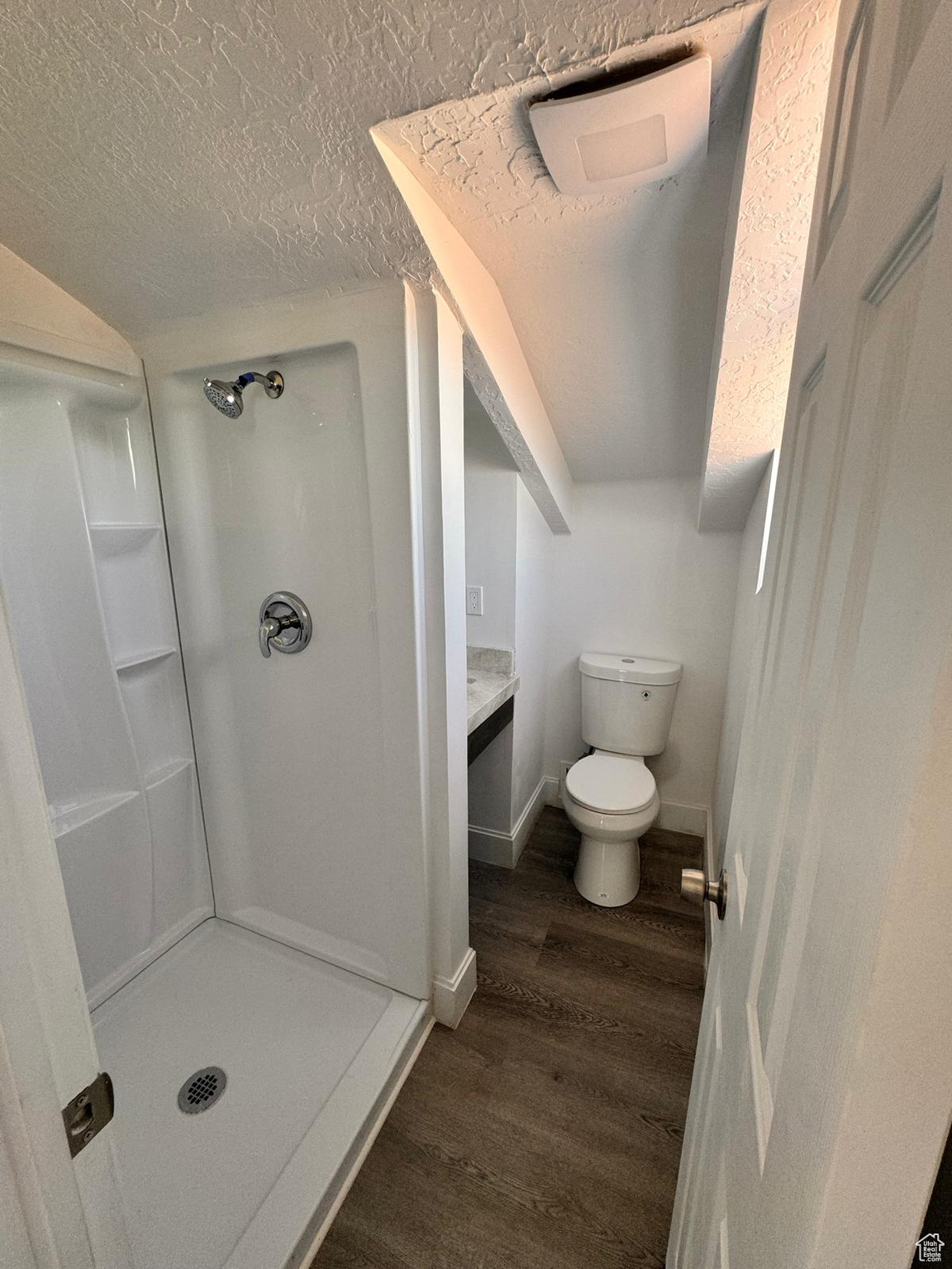 Bathroom featuring walk in shower, a textured ceiling, hardwood / wood-style flooring, vanity, and toilet