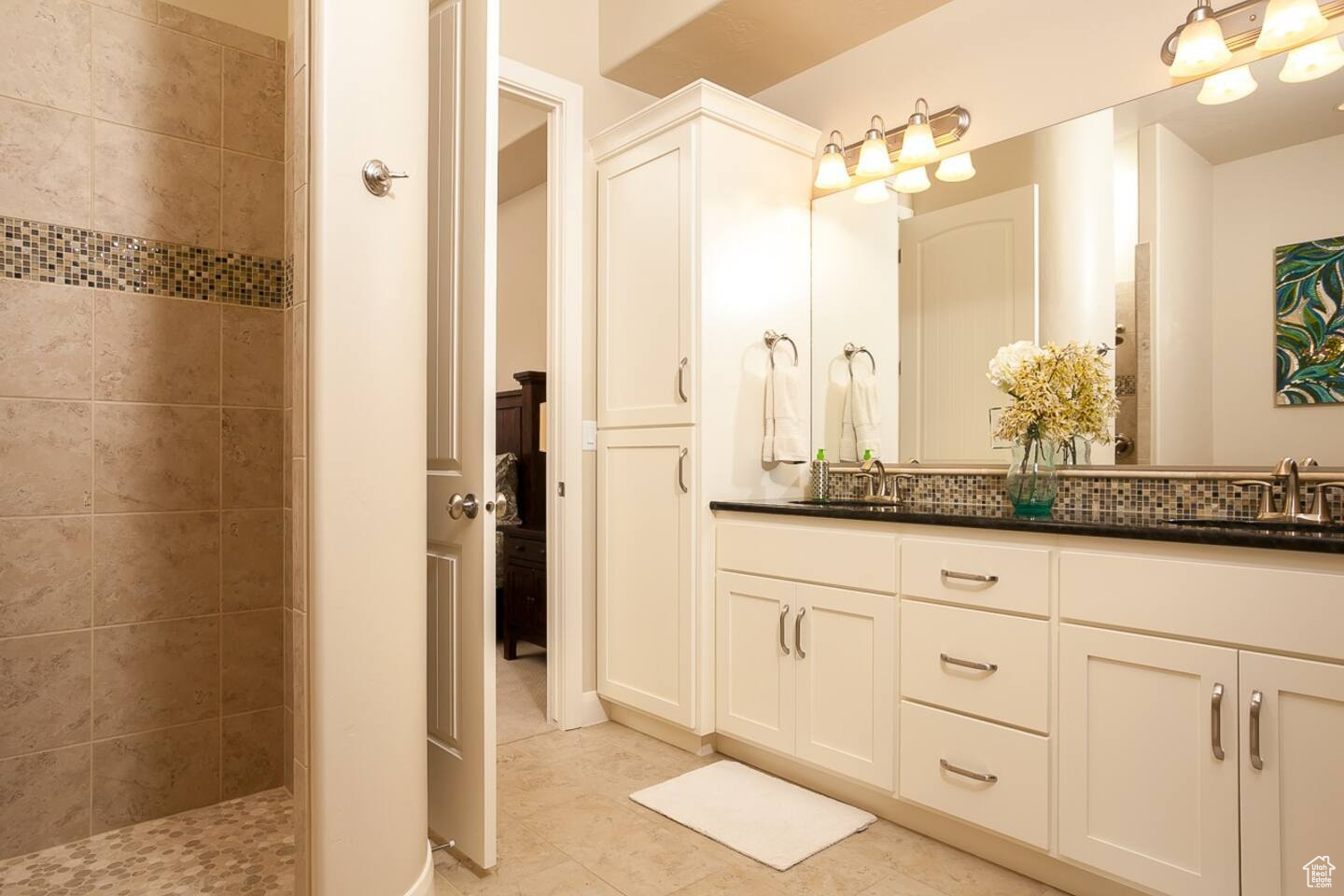 Bathroom featuring tiled shower, tile floors, oversized vanity, and dual sinks