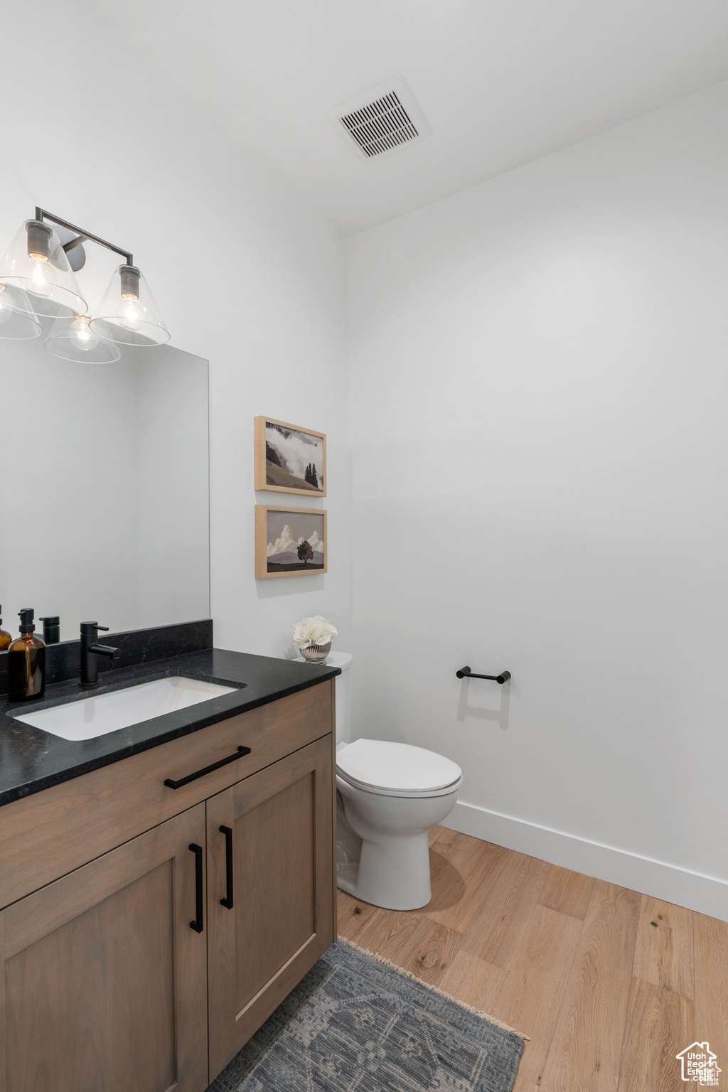 Main level half bath with wood-type flooring, vanity, and toilet