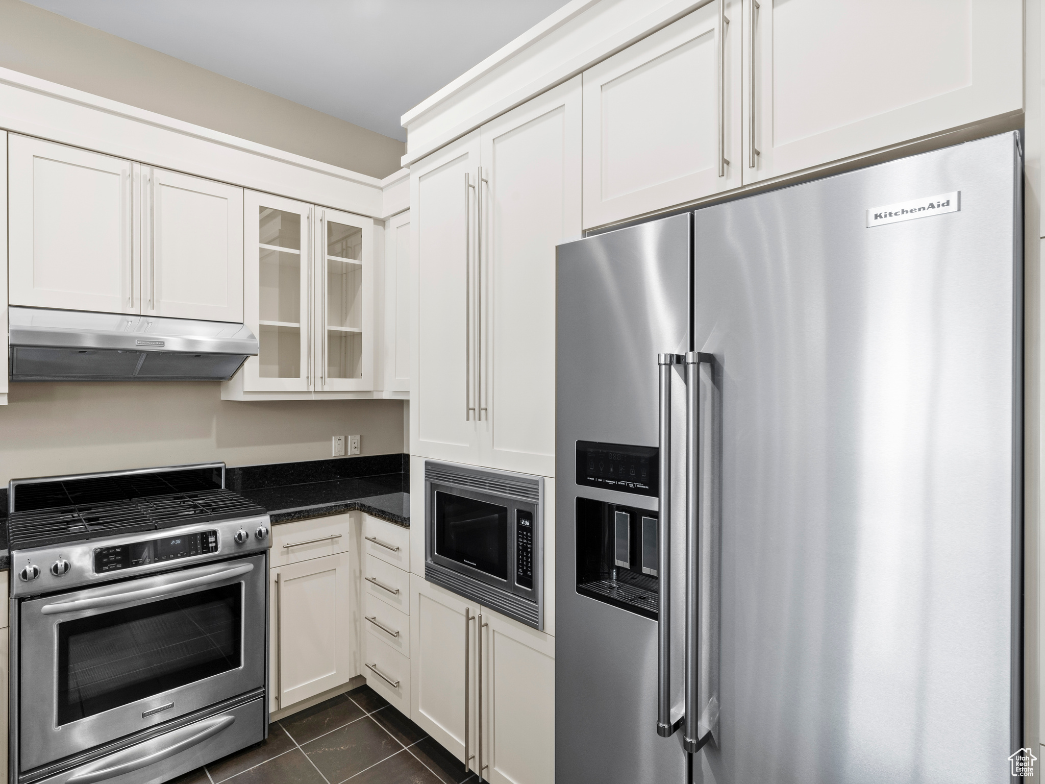 Kitchen featuring dark stone countertops, white cabinets, dark tile floors, and appliances with stainless steel finishes