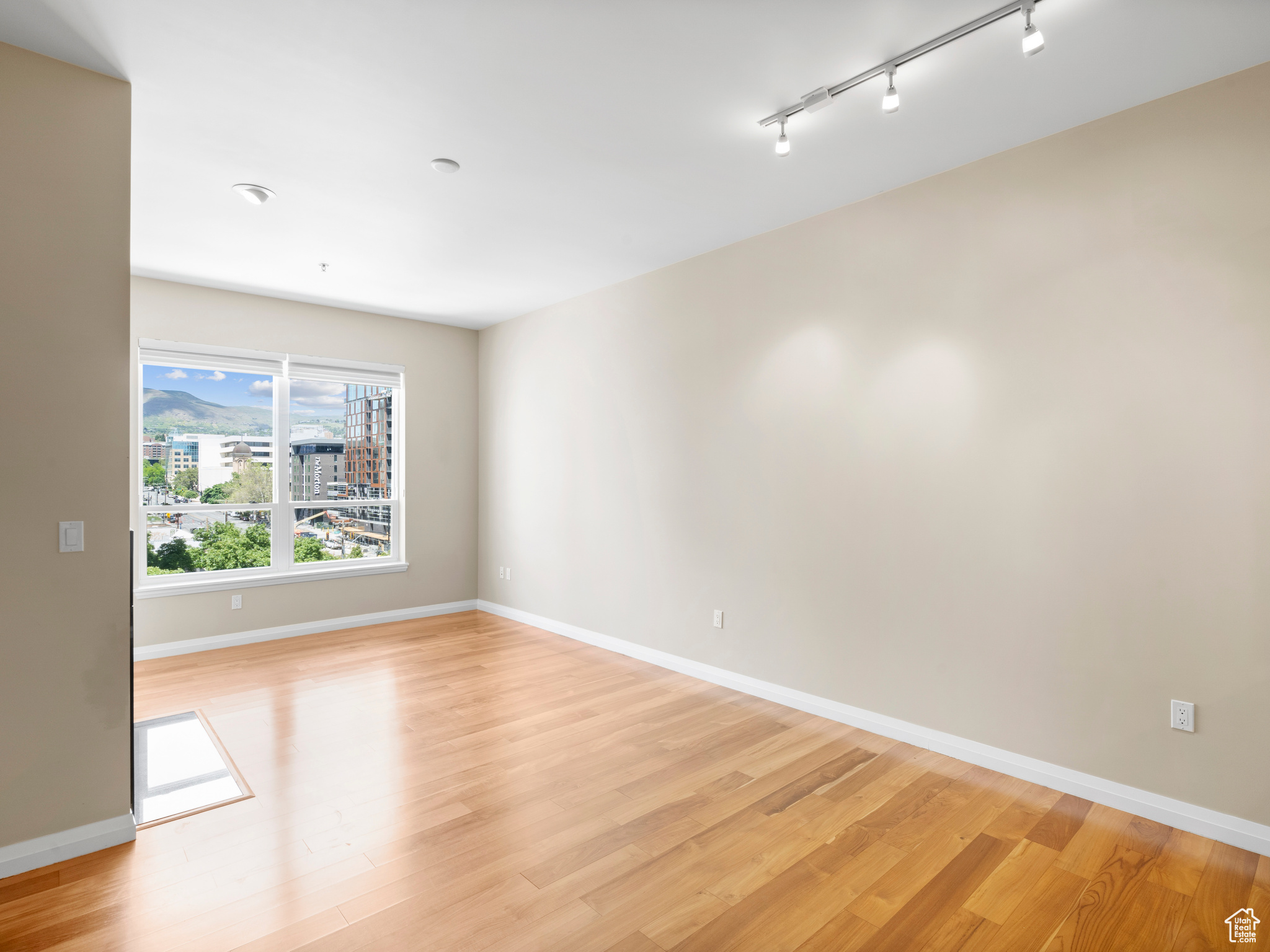 Empty room with light hardwood / wood-style floors and rail lighting