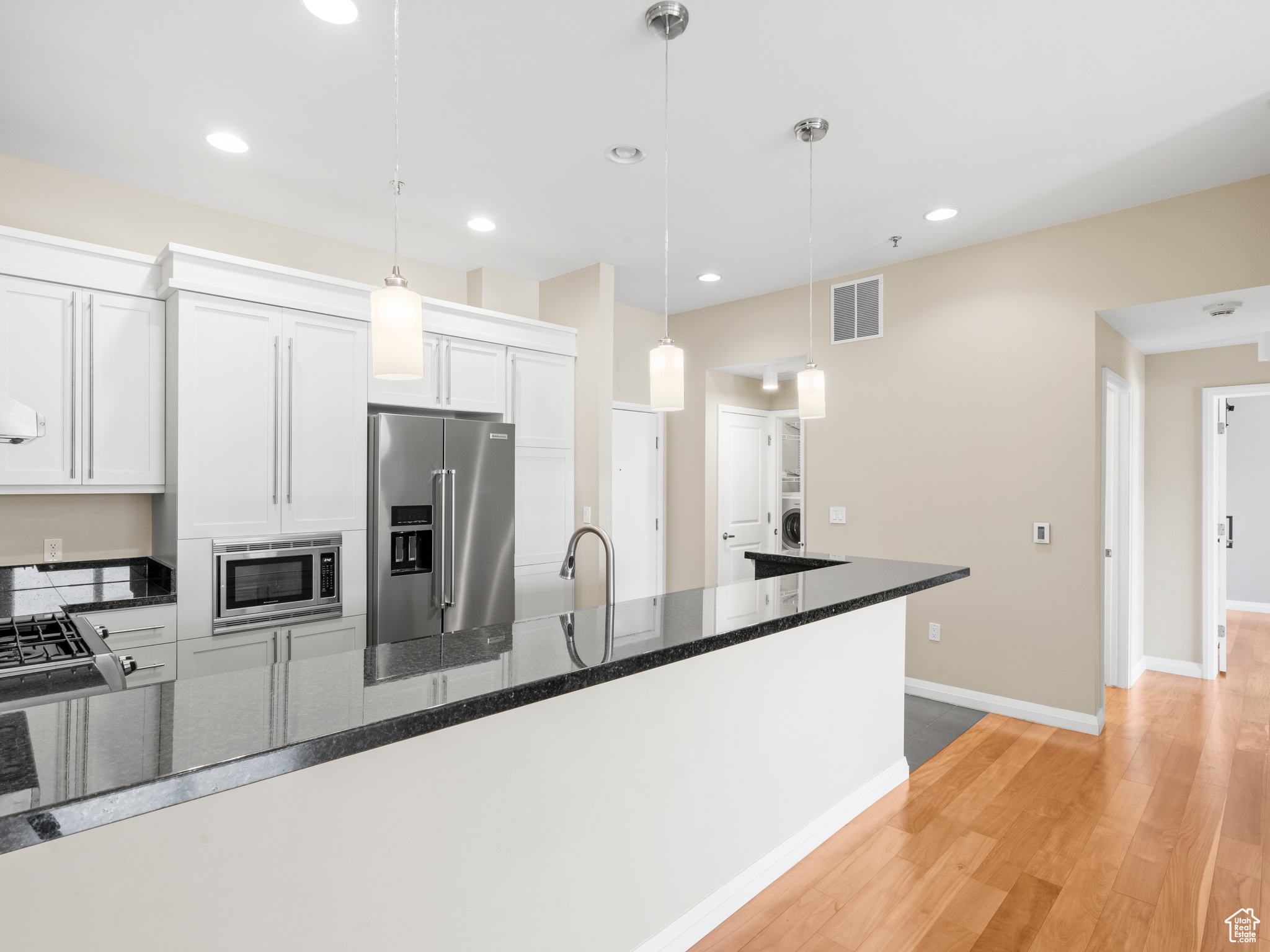 Kitchen with light hardwood / wood-style floors, white cabinetry, dark stone countertops, appliances with stainless steel finishes, and decorative light fixtures