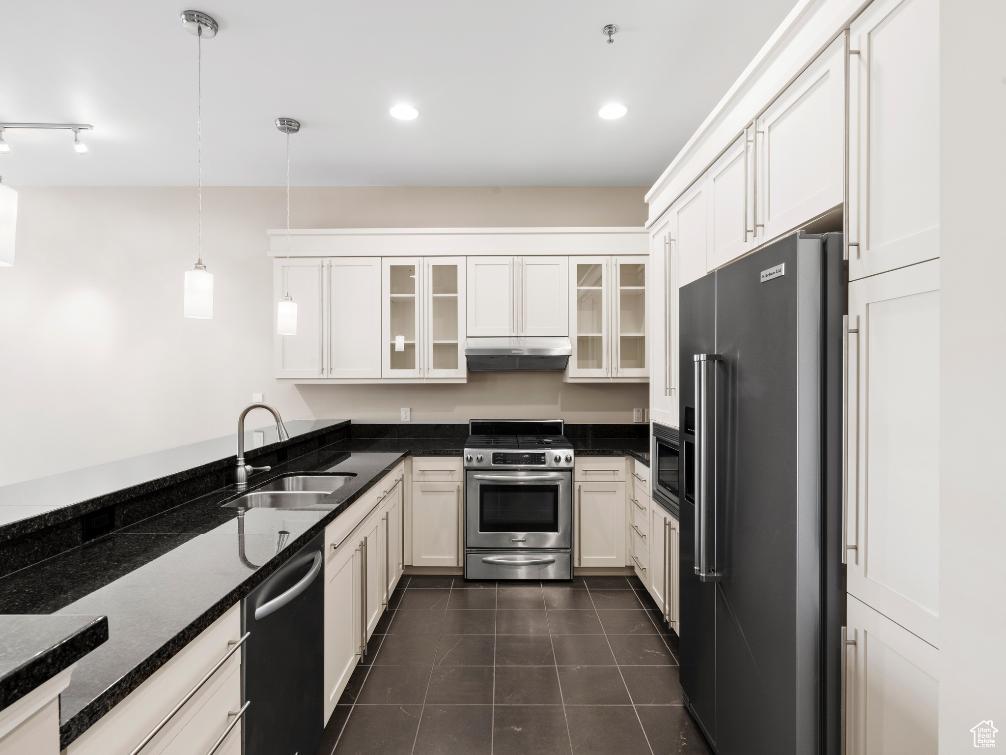 Kitchen with stainless steel appliances, white cabinets, decorative light fixtures, sink, and dark tile flooring