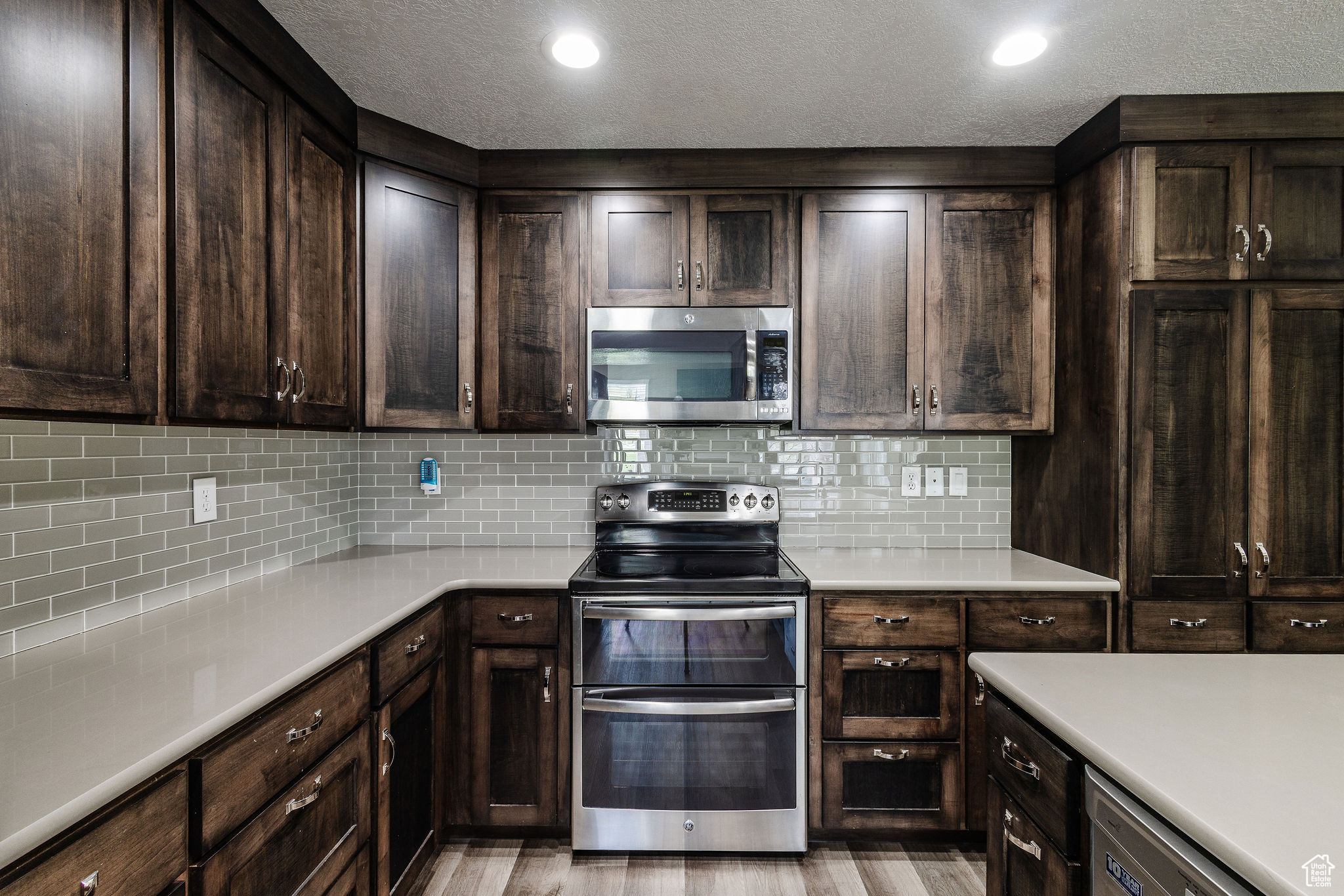 Kitchen featuring a textured ceiling, light hardwood / wood-style flooring, appliances with stainless steel finishes, backsplash, and dark brown cabinetry