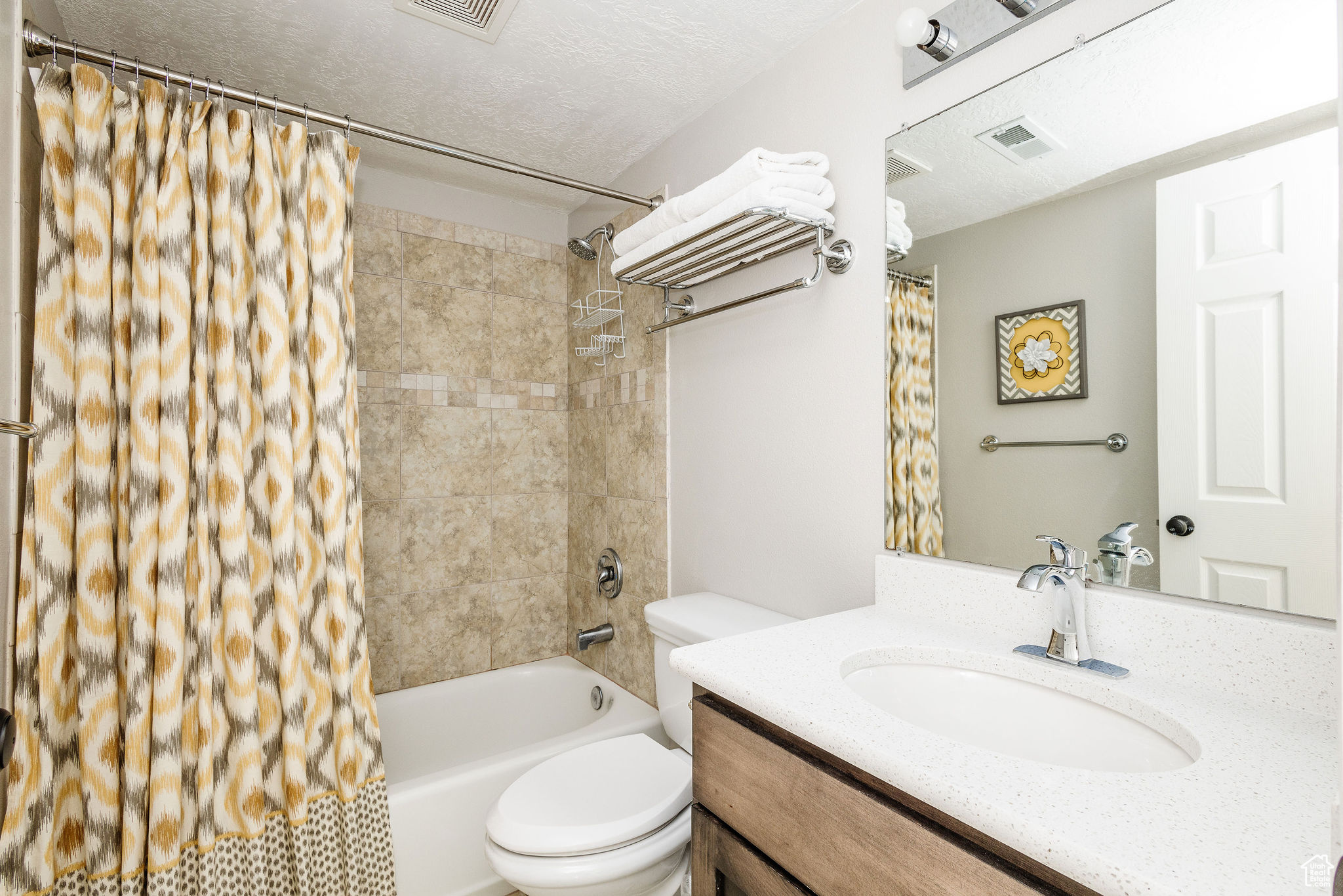 Full bathroom with shower / bathtub combination with curtain, vanity, toilet, and a textured ceiling